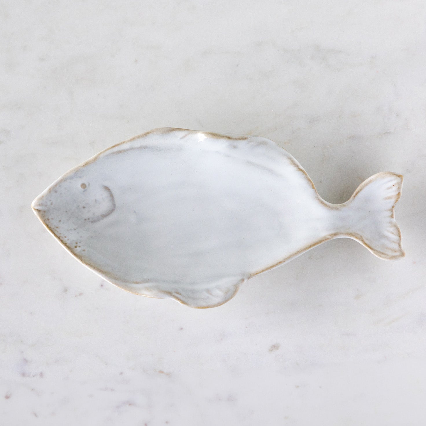 A stoneware, fish shaped dish with white reactive glaze, on a marble table.