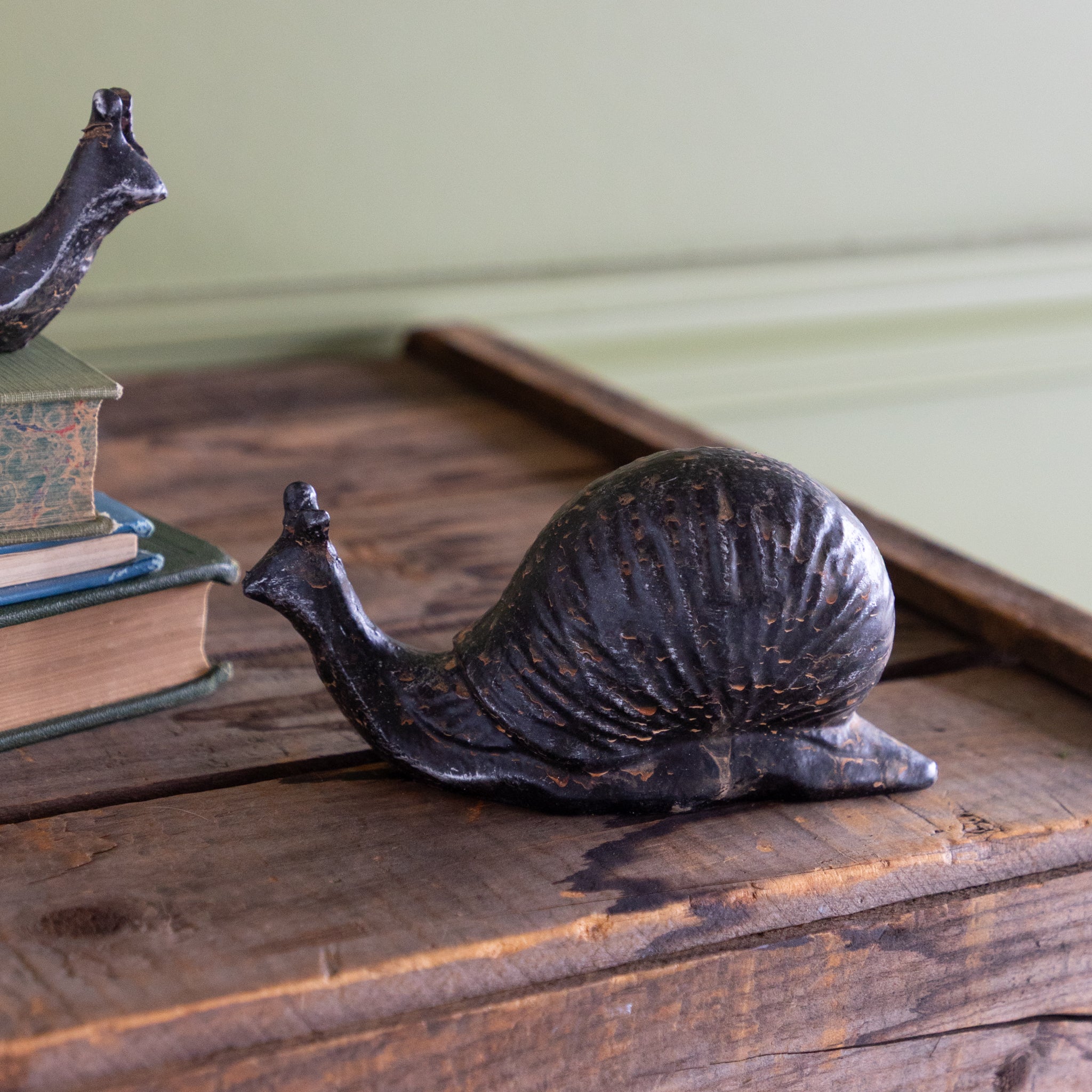 Decorative metal snail sculpture on a wooden surface with books in the background.