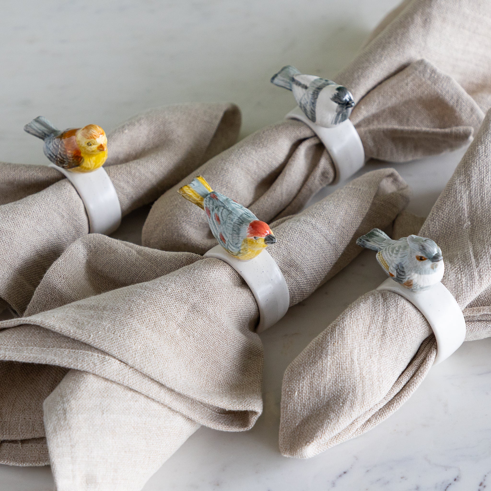 Stoneware Napkin Rings w/ Perched Bird around beige napkins.