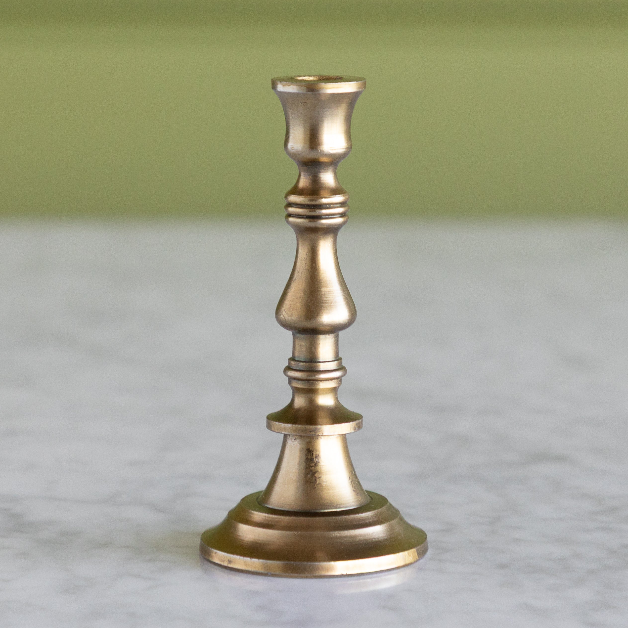 Brass candlestick on a marble surface with a green background.
