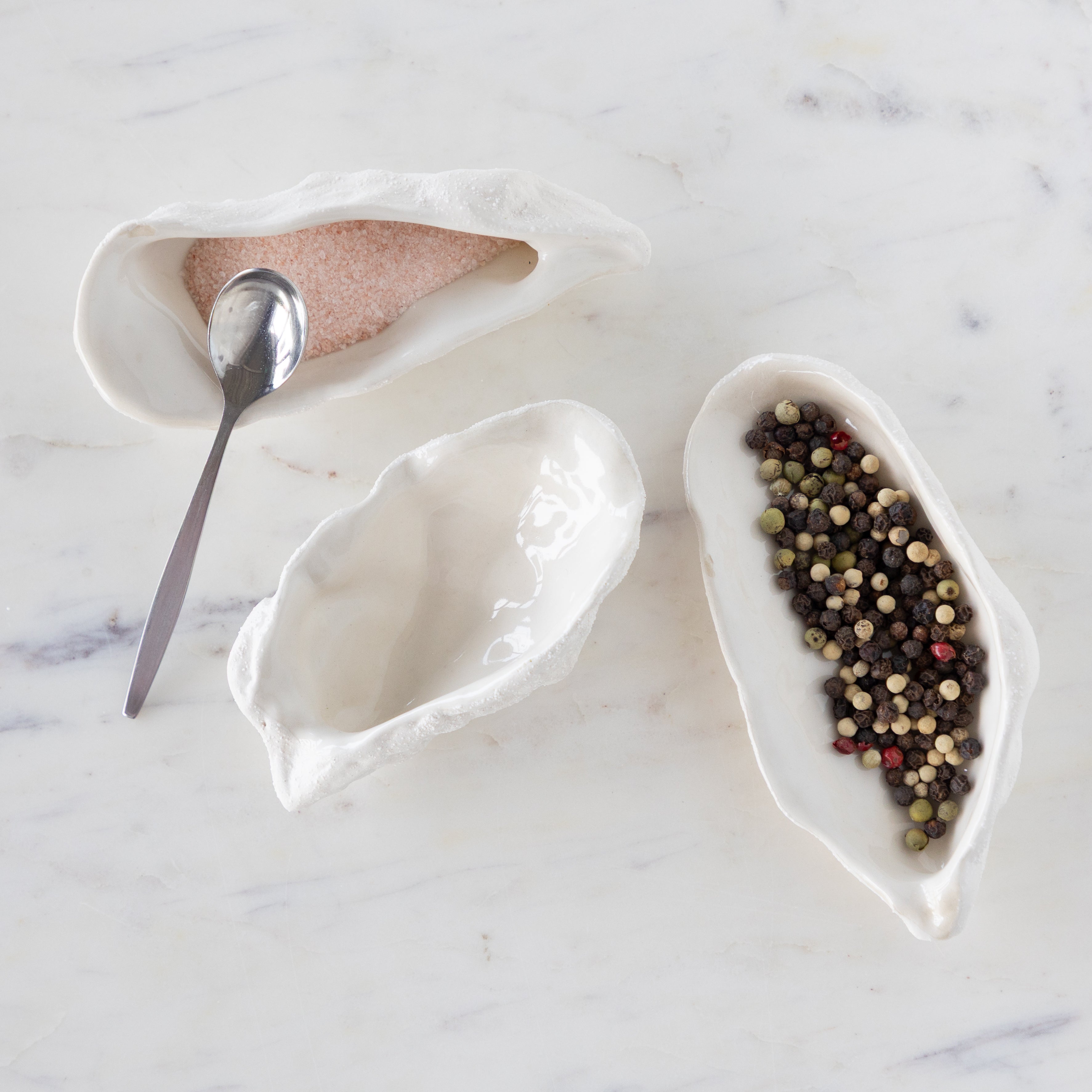 White ceramic oyster-shaped bowls with a spoon on a marble surface.