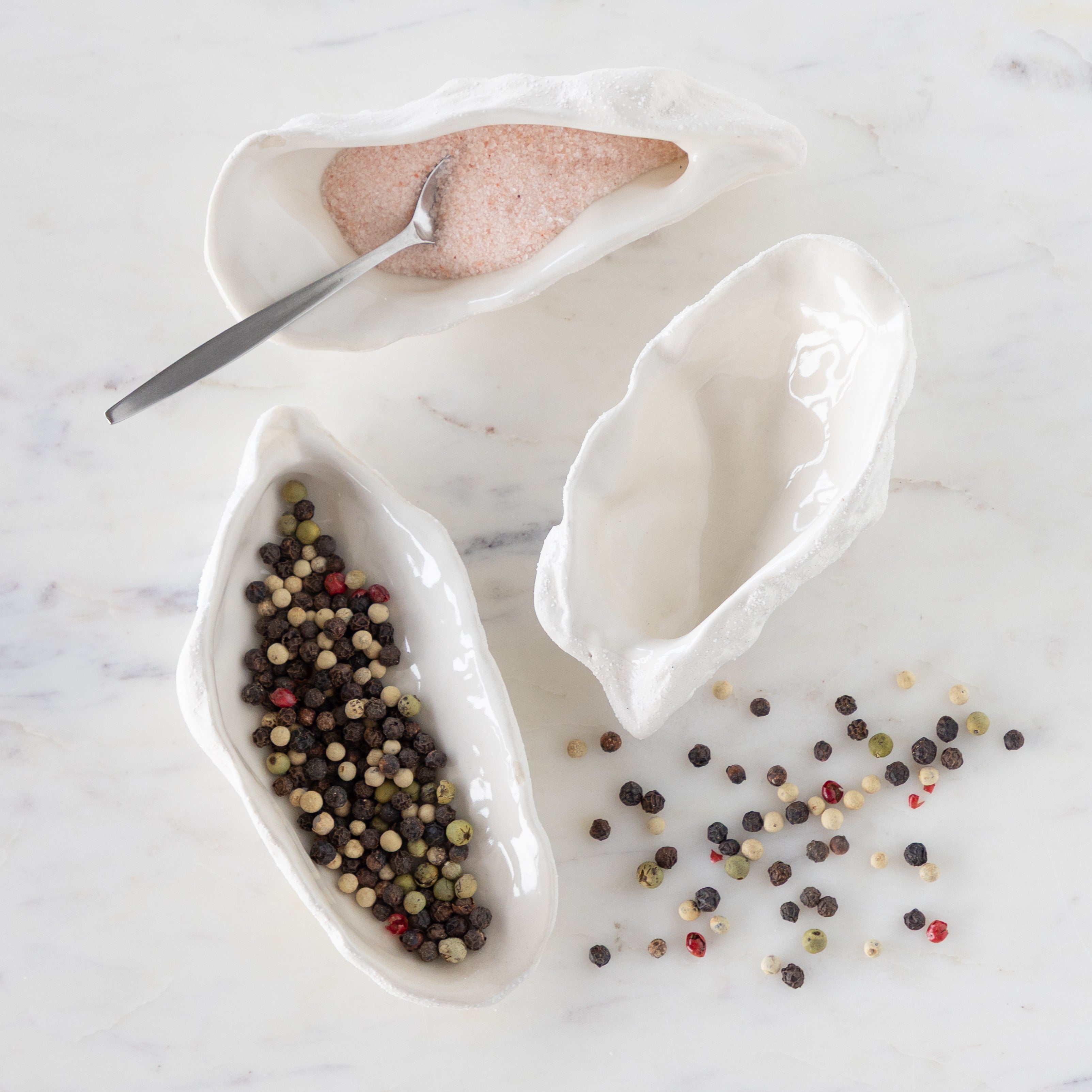 White ceramic oyster-shaped bowls with a spoon on a marble surface.
