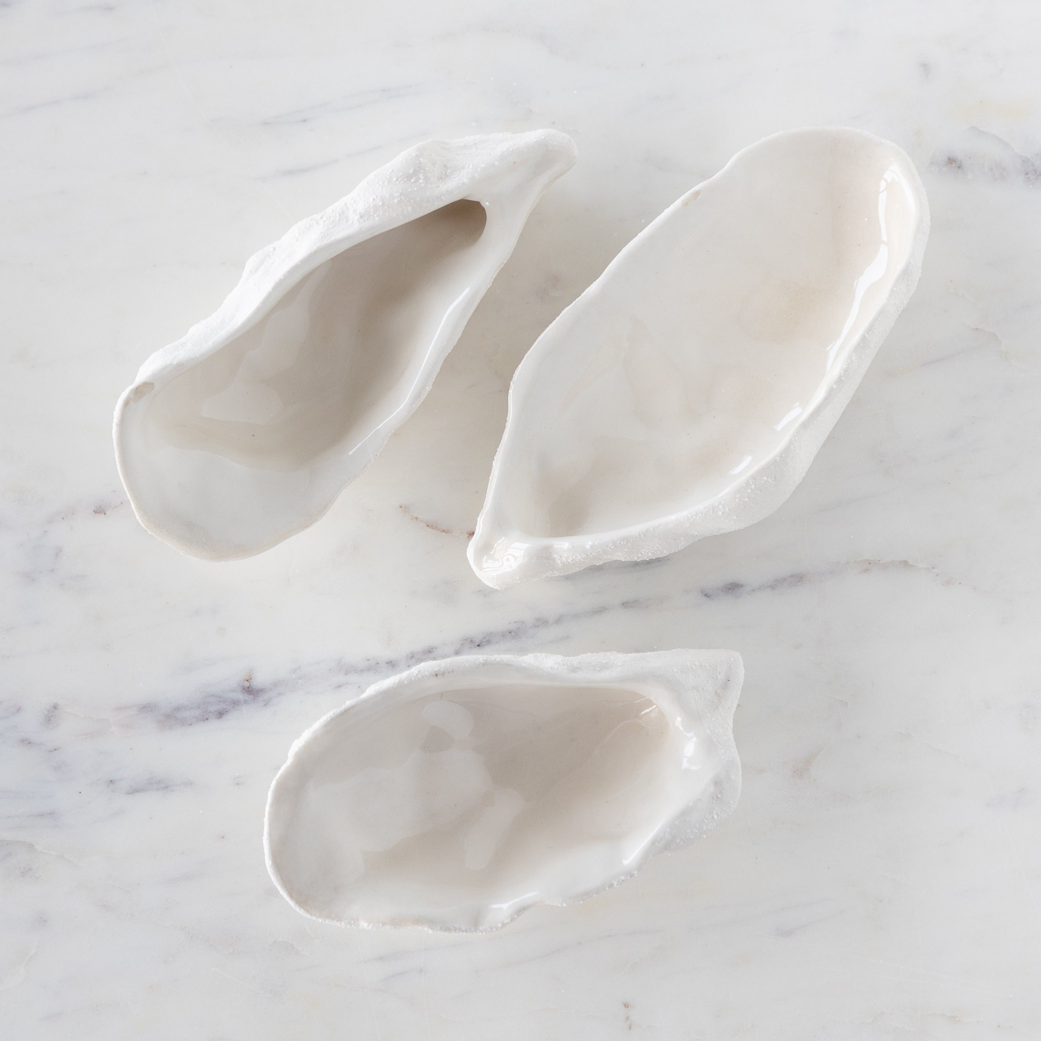 Three white ceramic shell-shaped dishes on a marble surface.