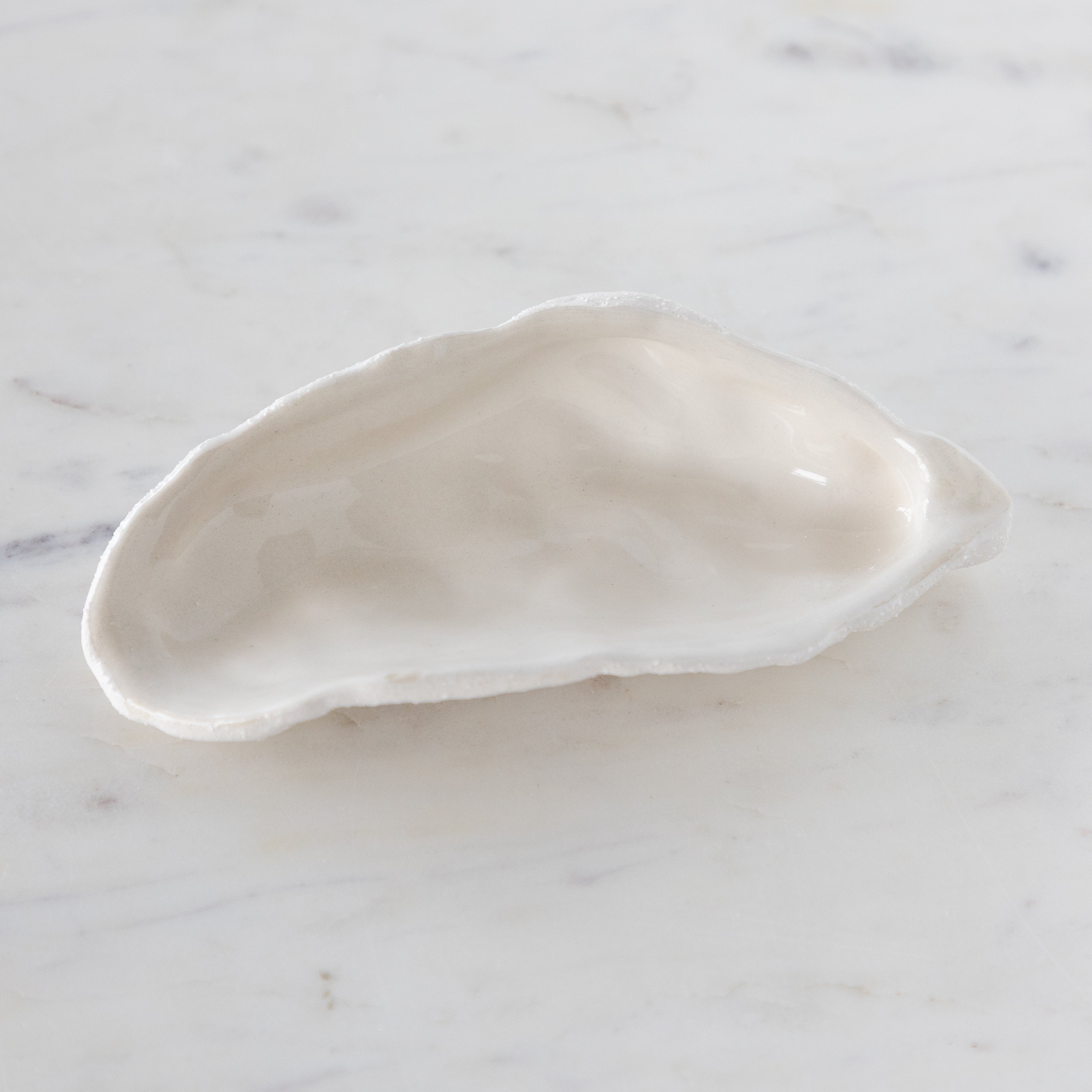 White ceramic oyster-shaped bowl on a marble surface.