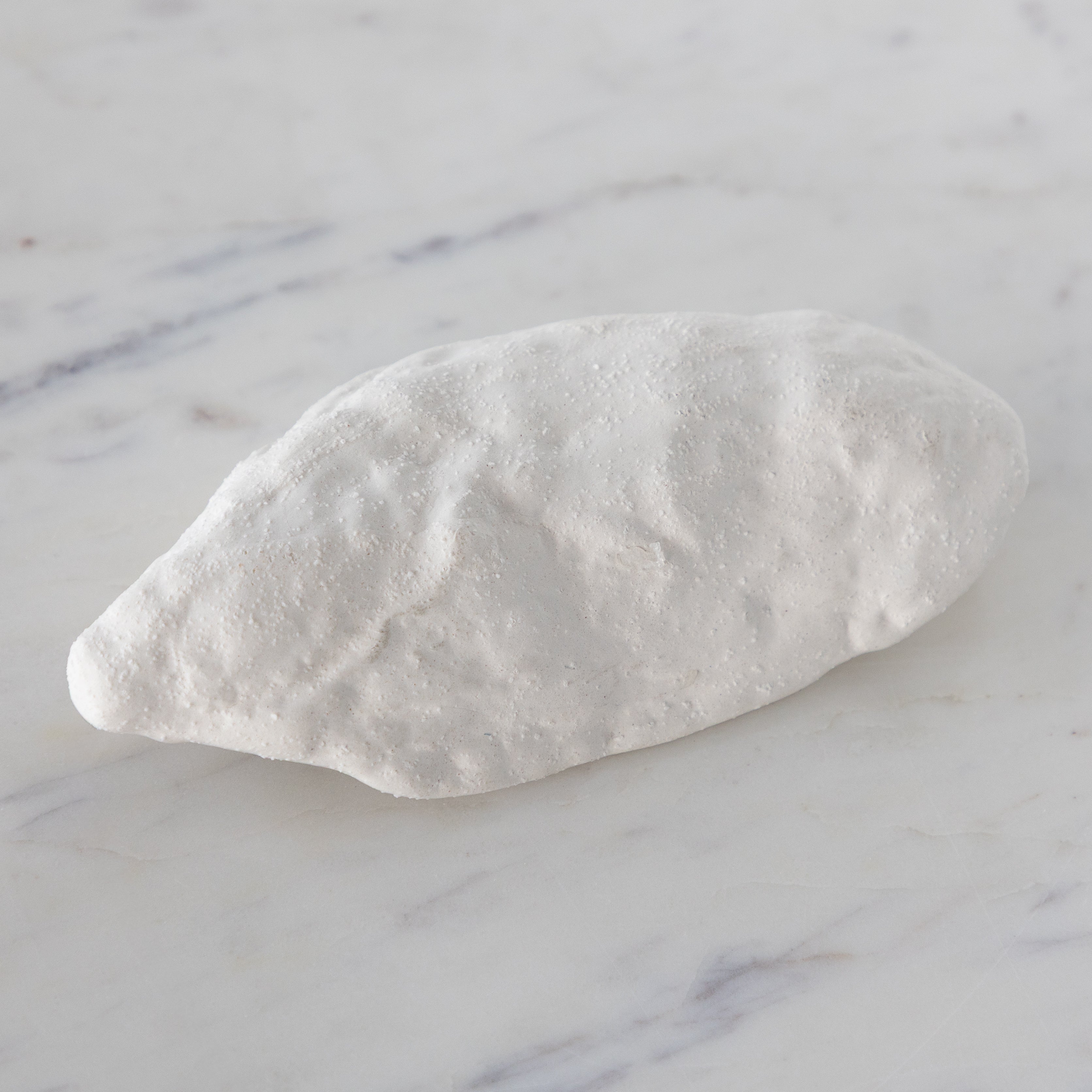 White ceramic oyster-shaped bowl on a marble surface.