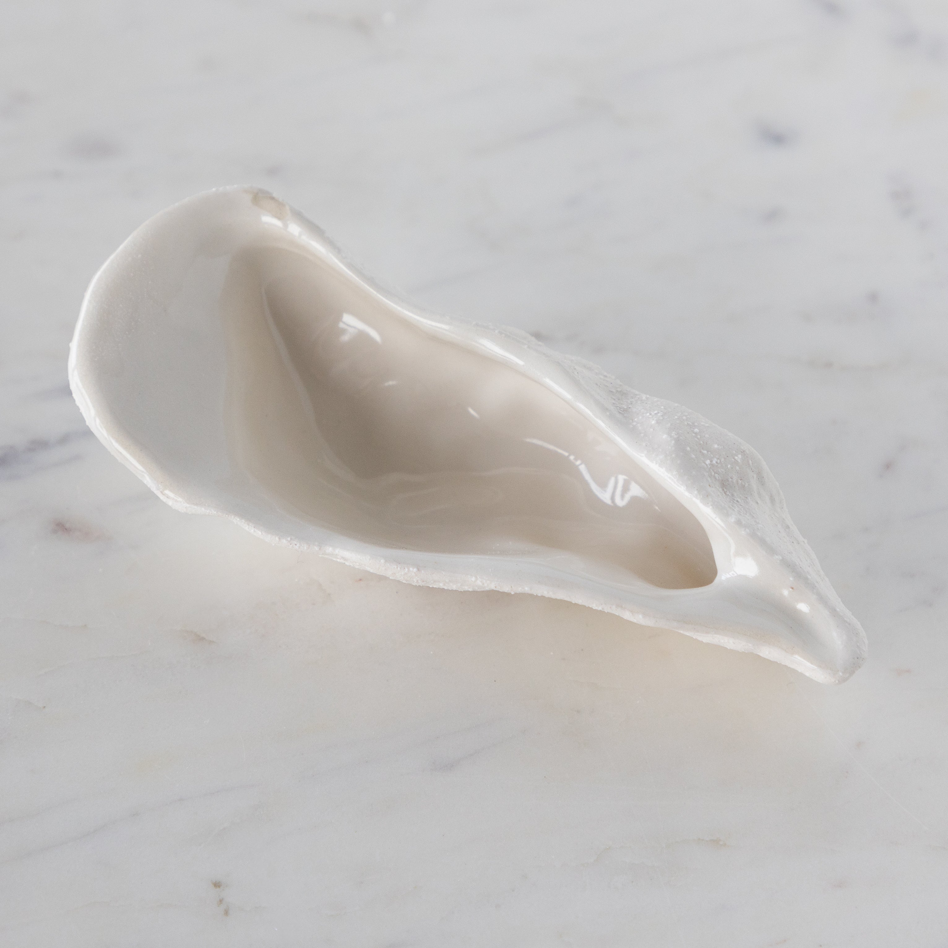 White ceramic oyster-shaped bowl on a marble surface.