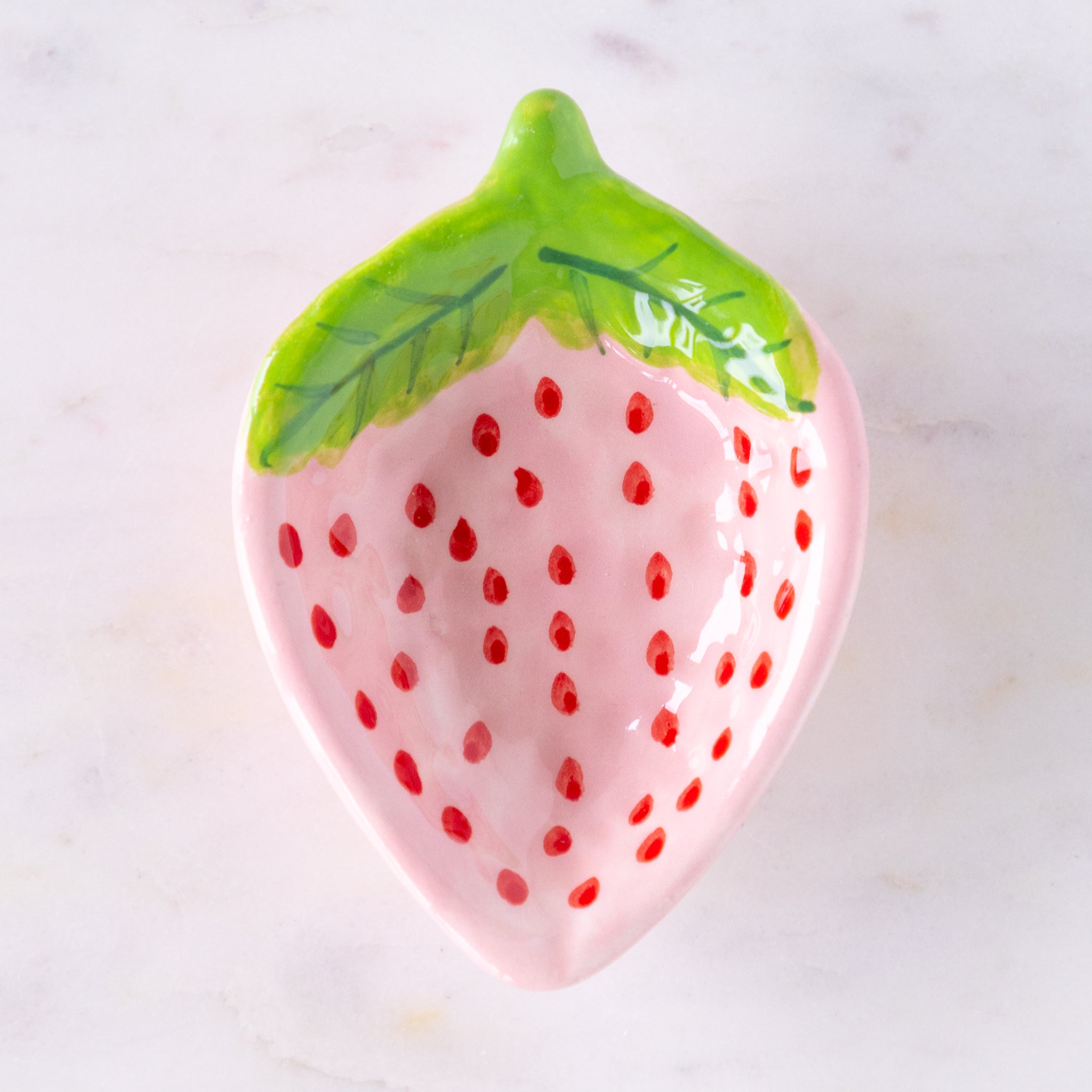 Pink strawberry-shaped dish with green leaf on a white background.