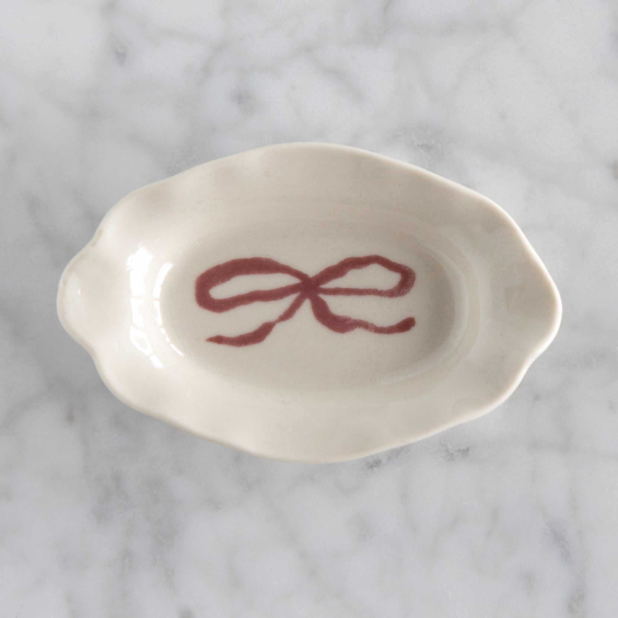 White ceramic dish with a red bow design on a marble surface.