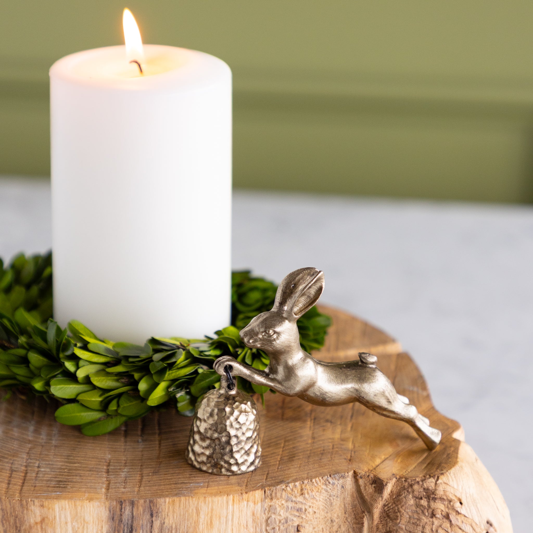 Candle with greenery and a gold rabbit candle snuffer on a wooden surface.