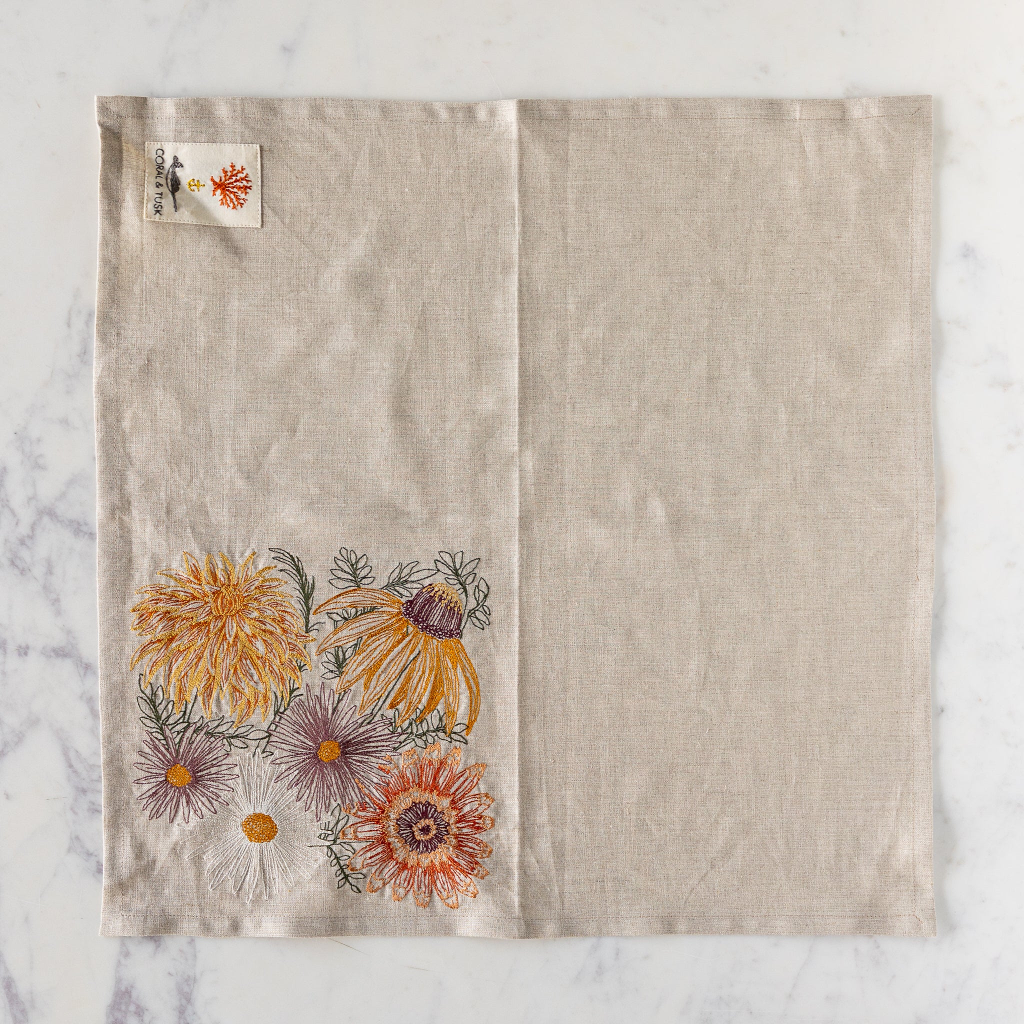 Autumn Blossoms Dinner Napkin unfolded on a table showing the design on one square and logo patch on another.
