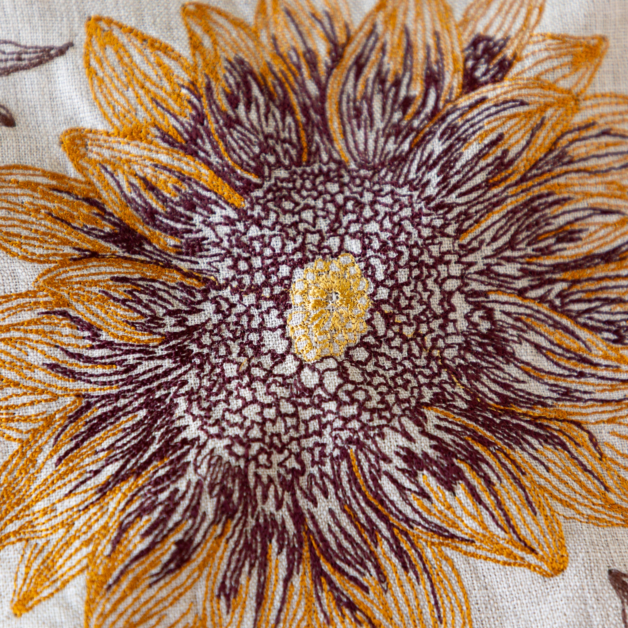Close-up of an embroidered sunflower pattern on fabric with brown and orange petals.