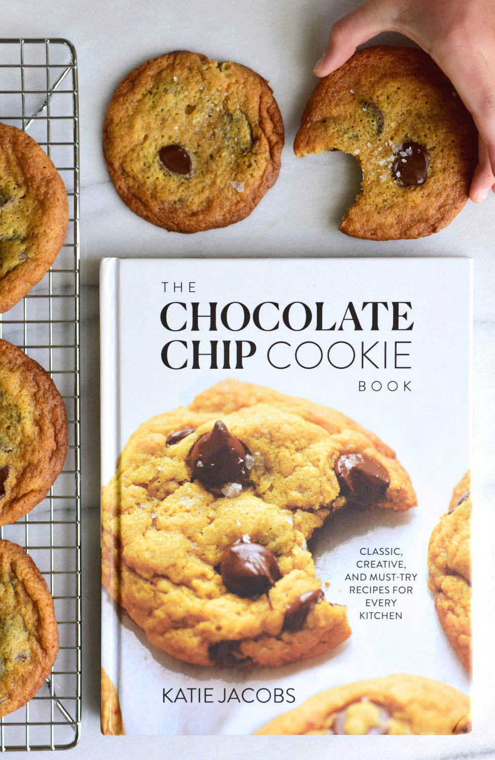 Chocolate Chip Cookie Book next to a rack of cooling cookies.