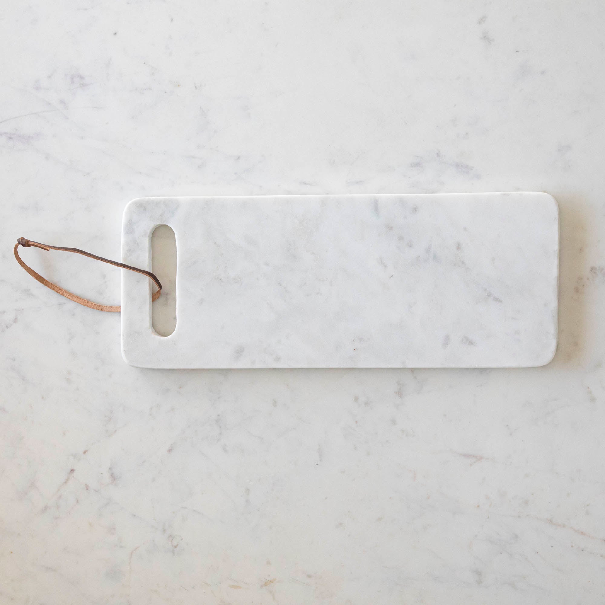 A White Marble Cheese Board with a cutout made for holding and a brown loop for decoration.