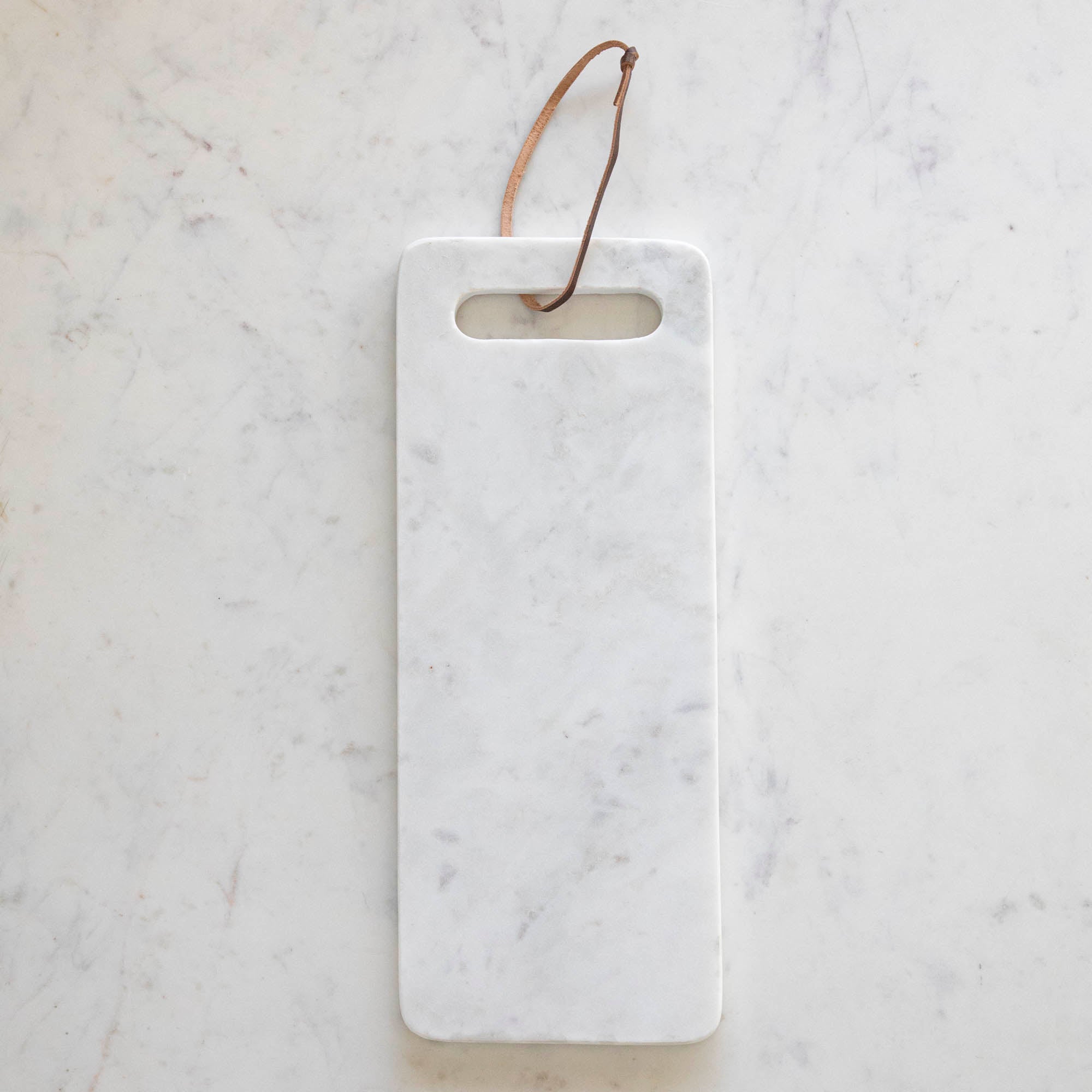A White Marble Cheese Board with a cutout made for holding and a brown loop for decoration.