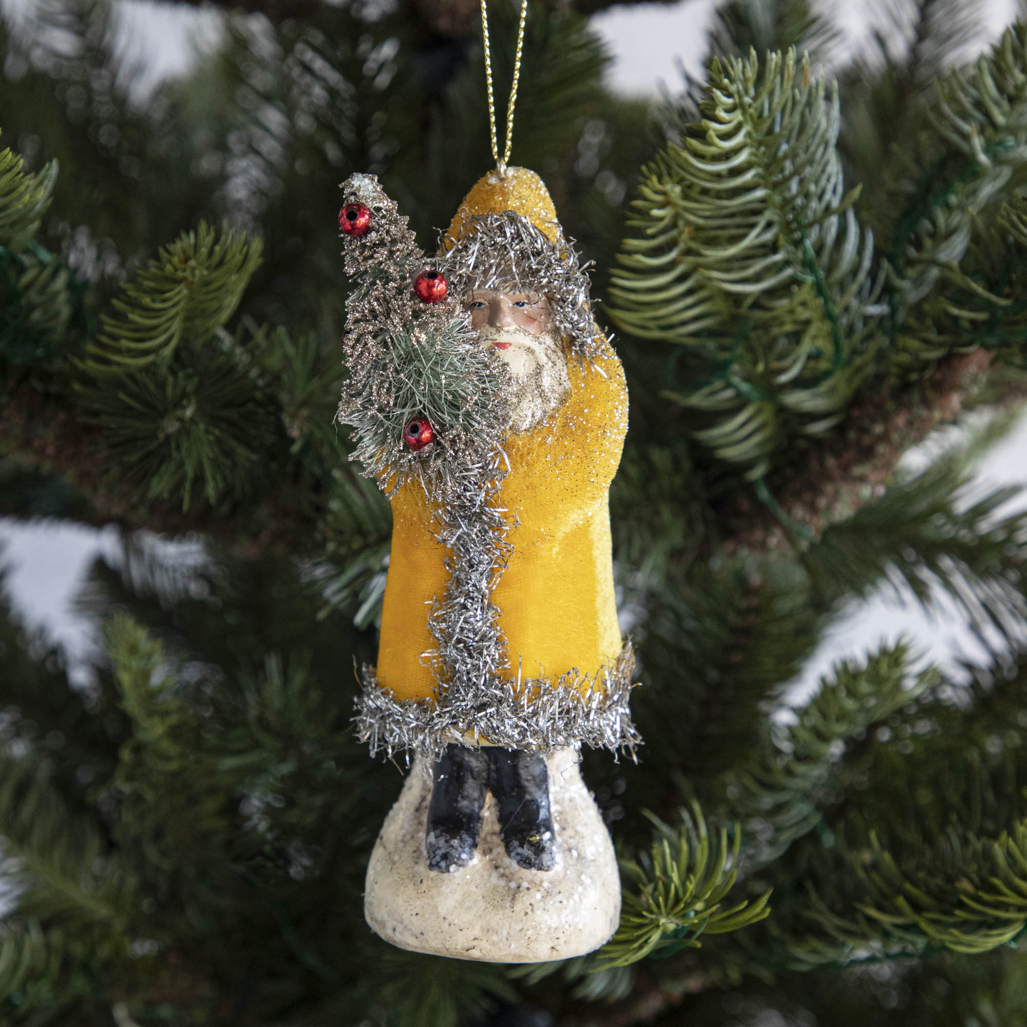 A yellow-robed Santa Claus ornament on a tree.