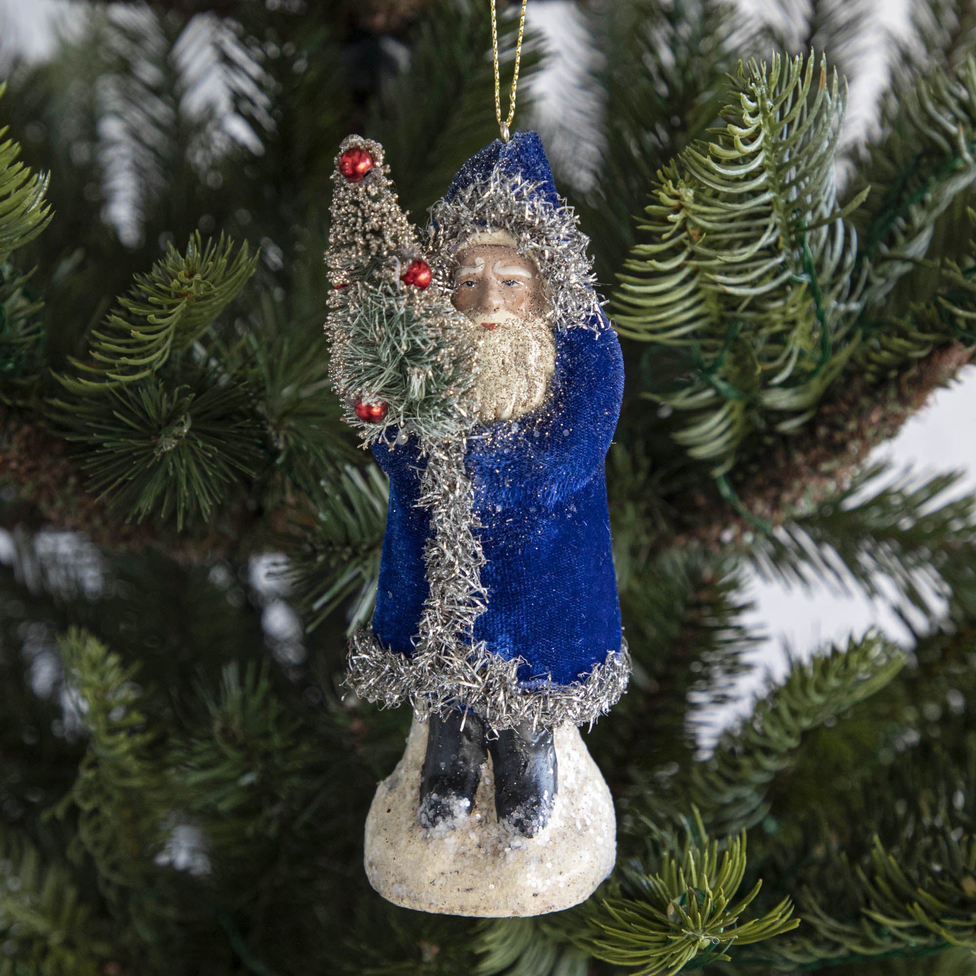 A blue-robed Santa Claus ornament on a tree.
