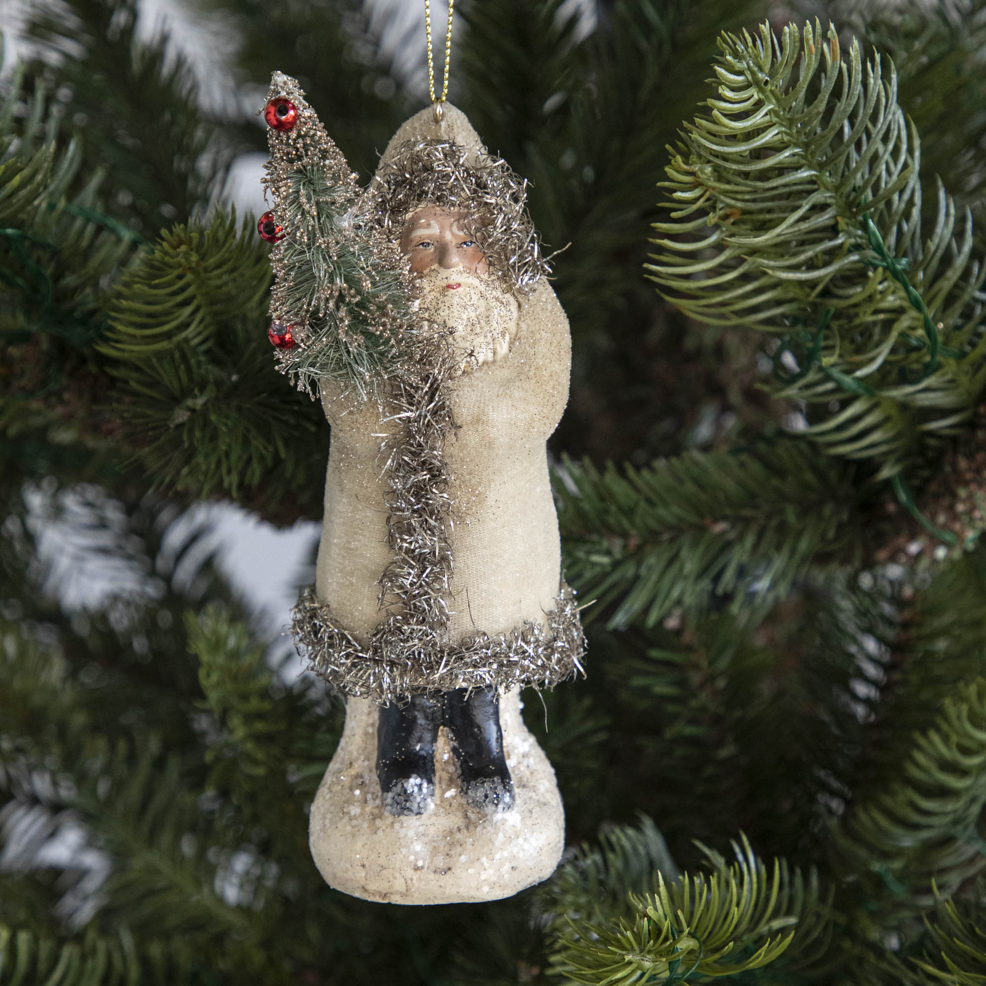 A cream-robed Santa Claus ornament on a tree.