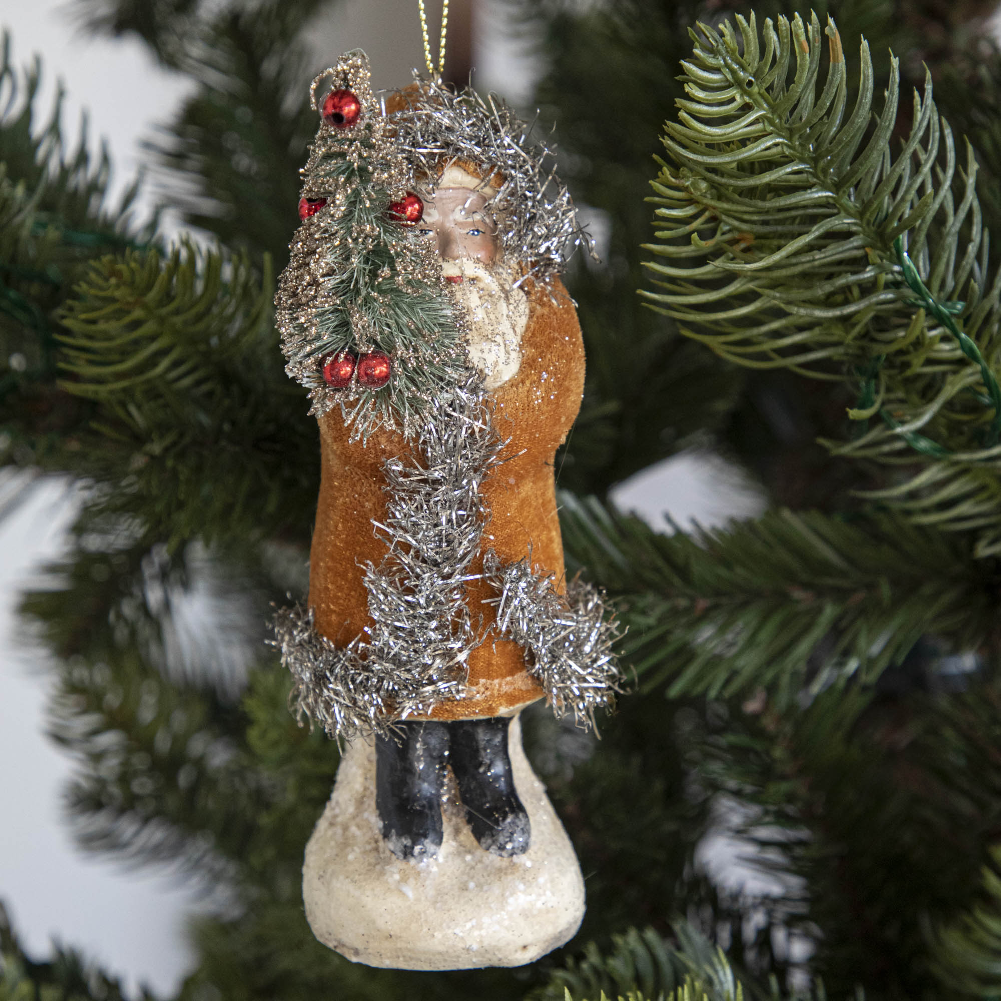 An orange-robed Santa Claus ornament on a tree.