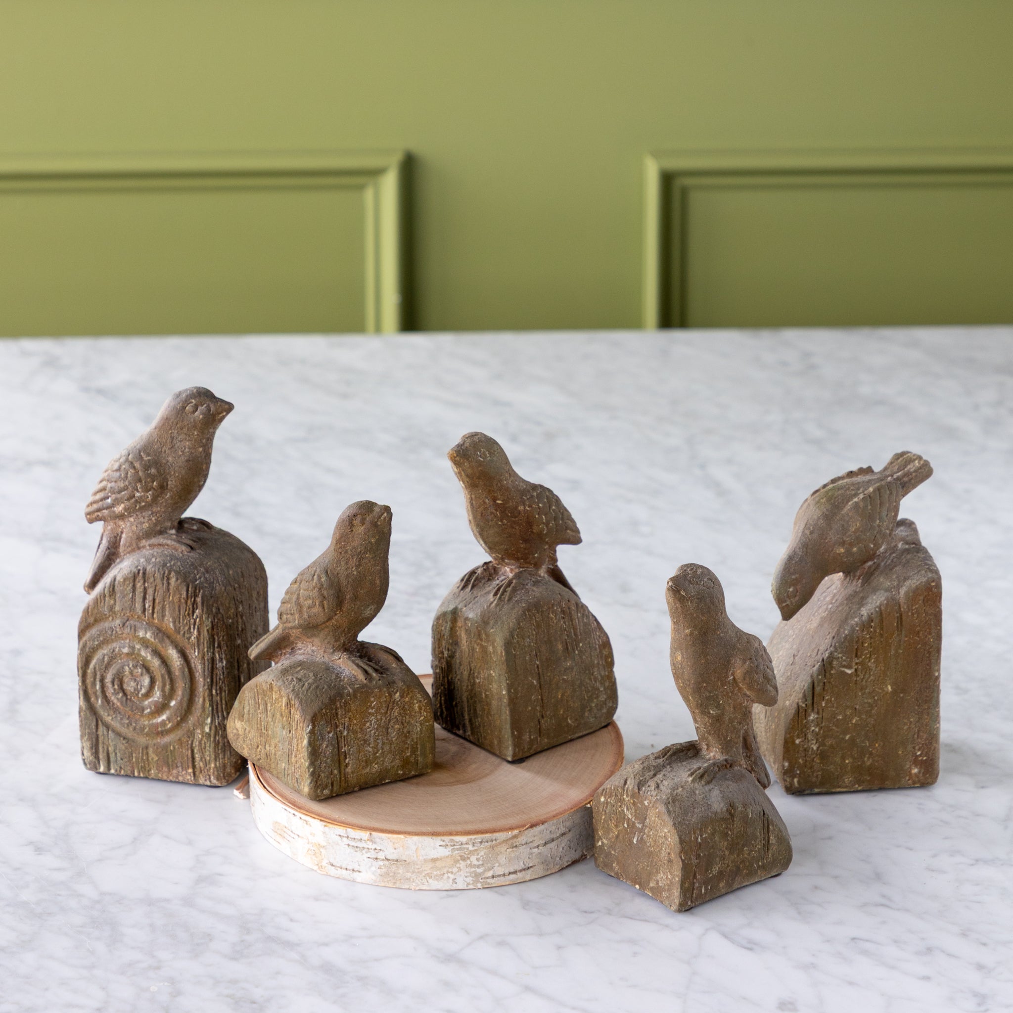 Set of wooden bird sculptures on a white surface with a green wall background.