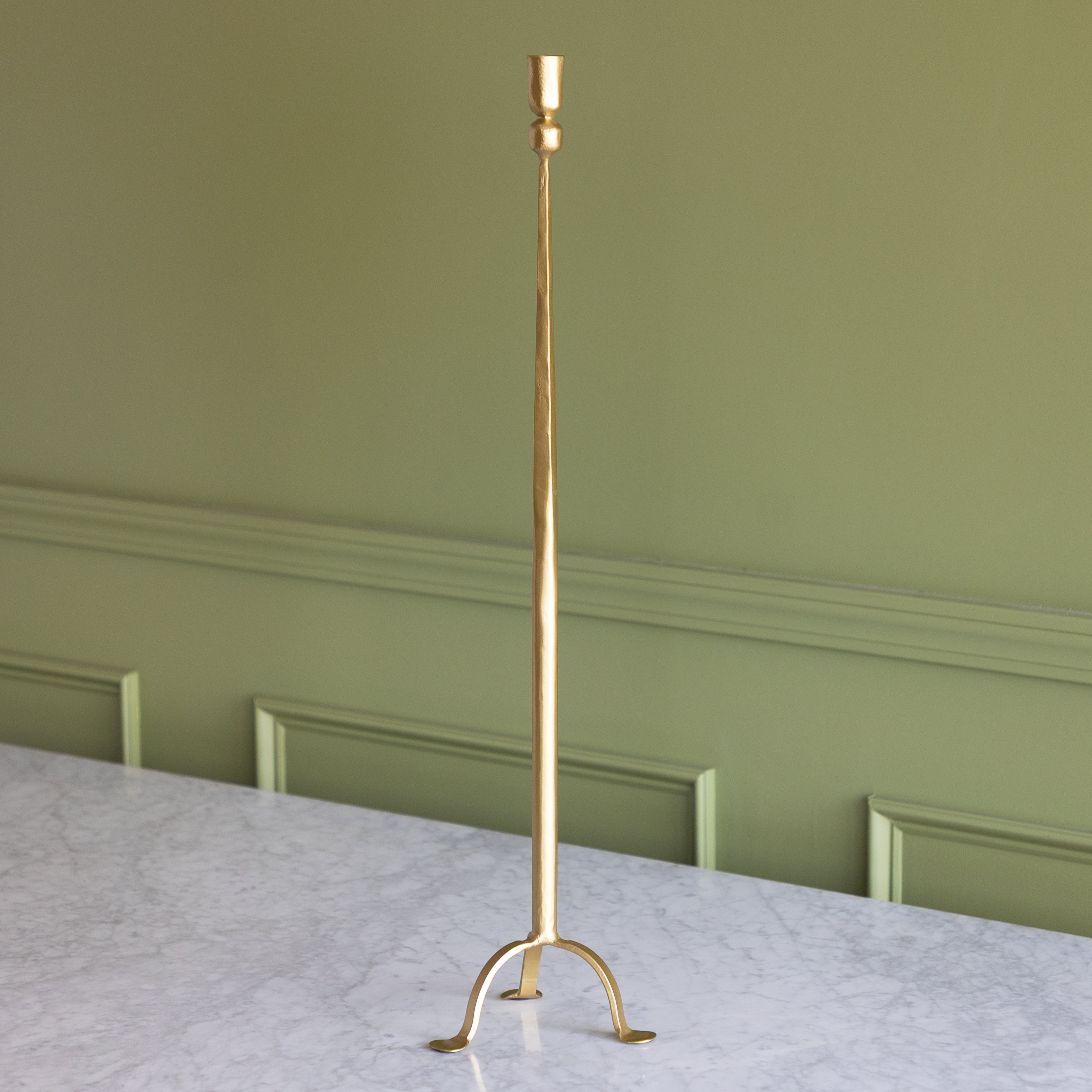Gold candlestick on a marble surface with a green wall background