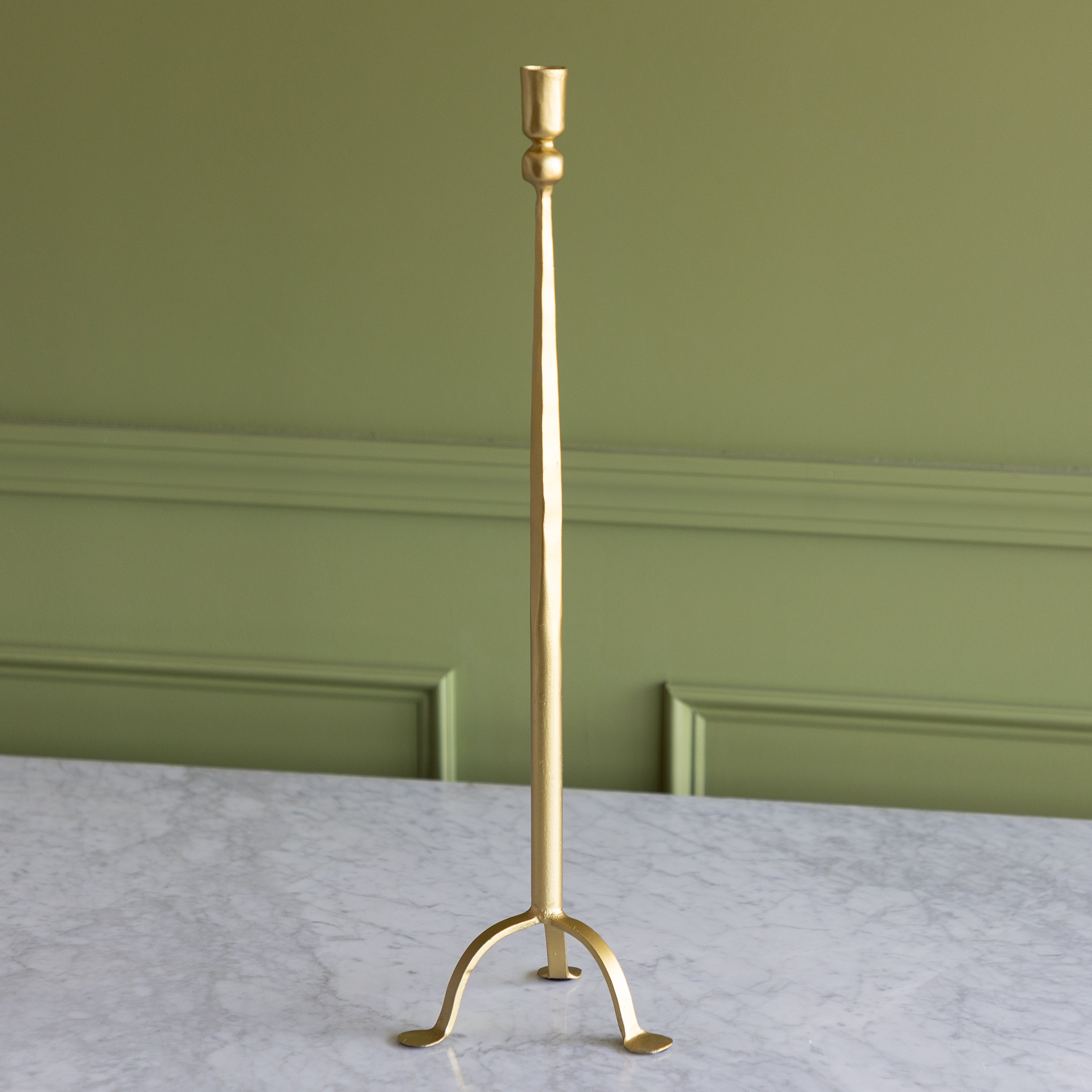 Gold candlestick holder on a marble surface with a green wall background