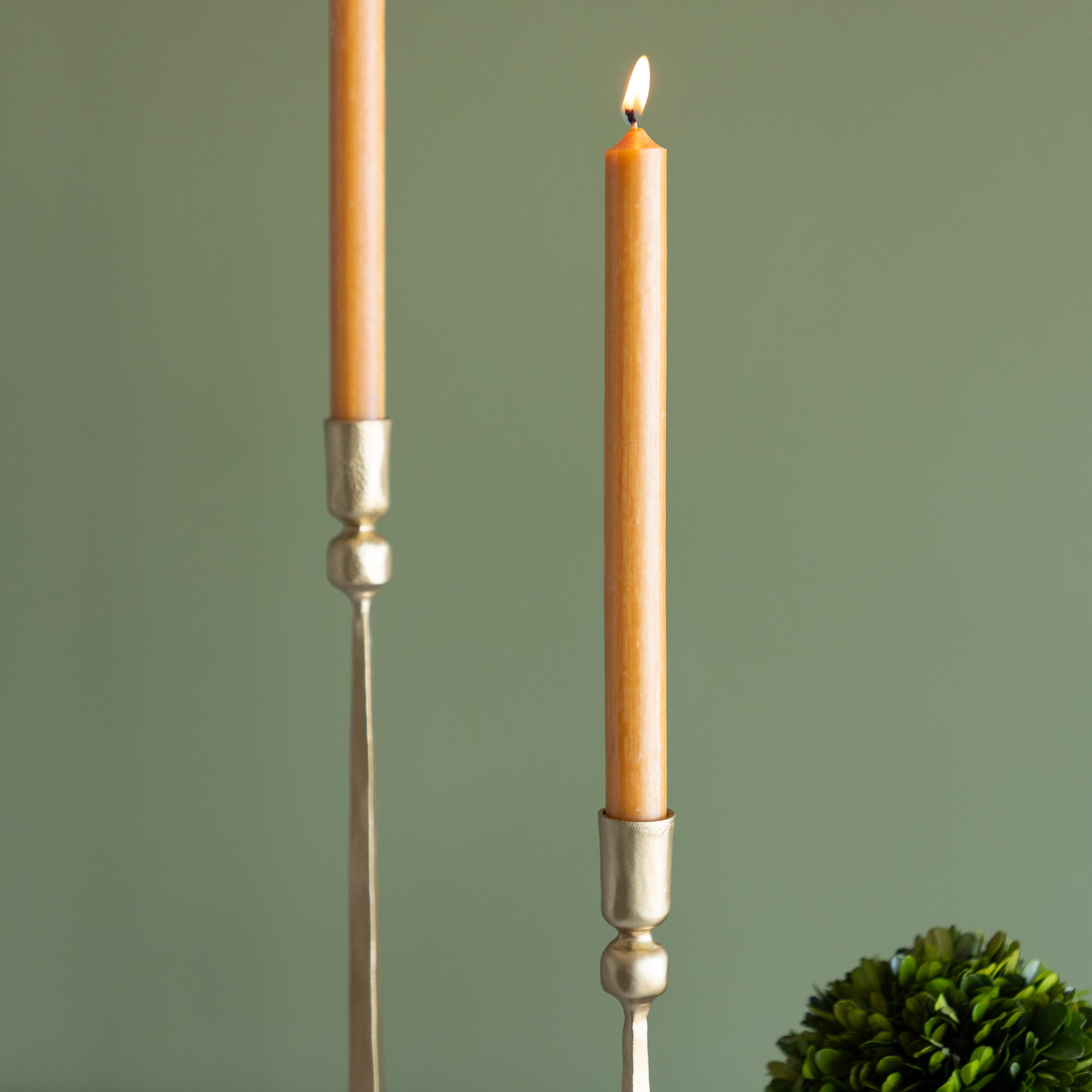 Two candles in decorative holders with a green background