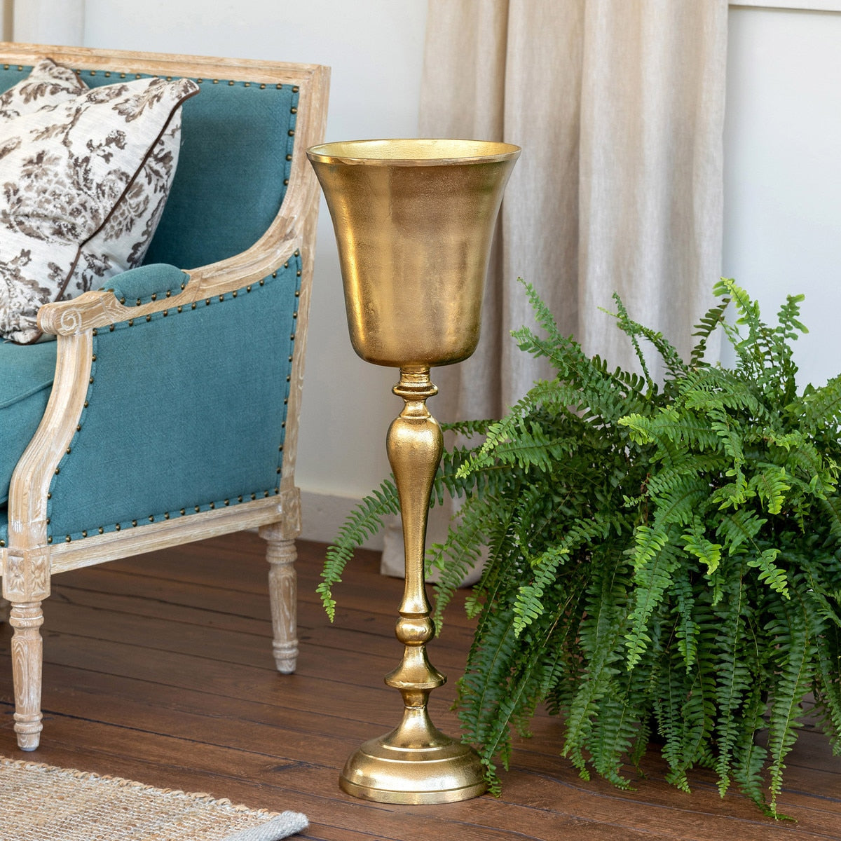 Gold bottle holder on a wooden floor with a teal chair and green plant in the background.