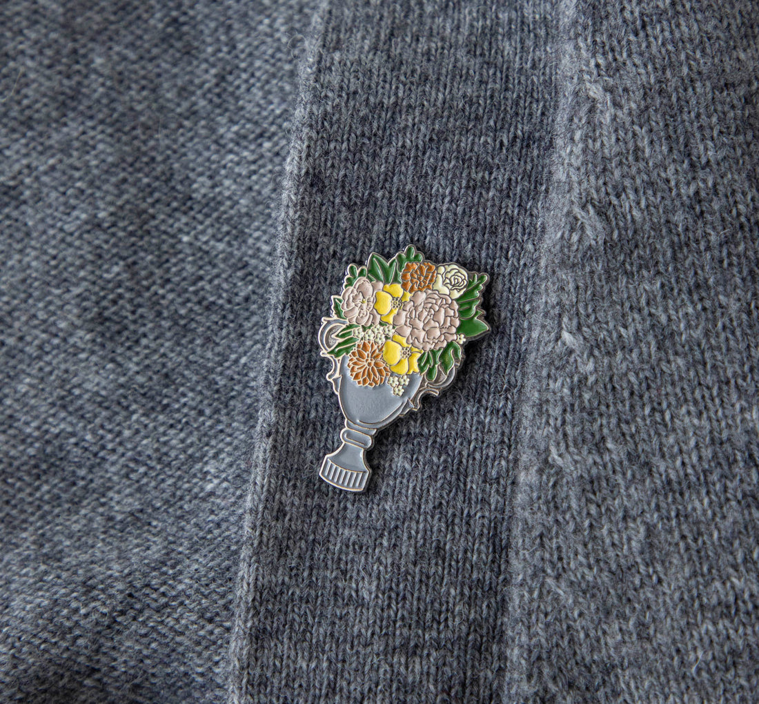 An Hester &amp; Cook enamel pin depicting a garden trophy with flowers in a vase, perfect for decorating a backpack.