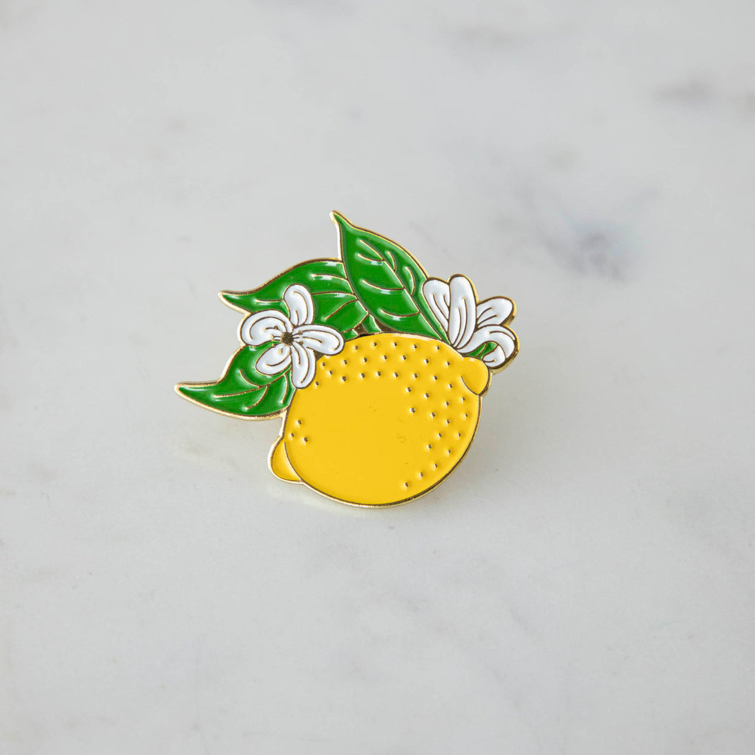 A Hester &amp; Cook Lemon Enamel Pin adorned with leaves.