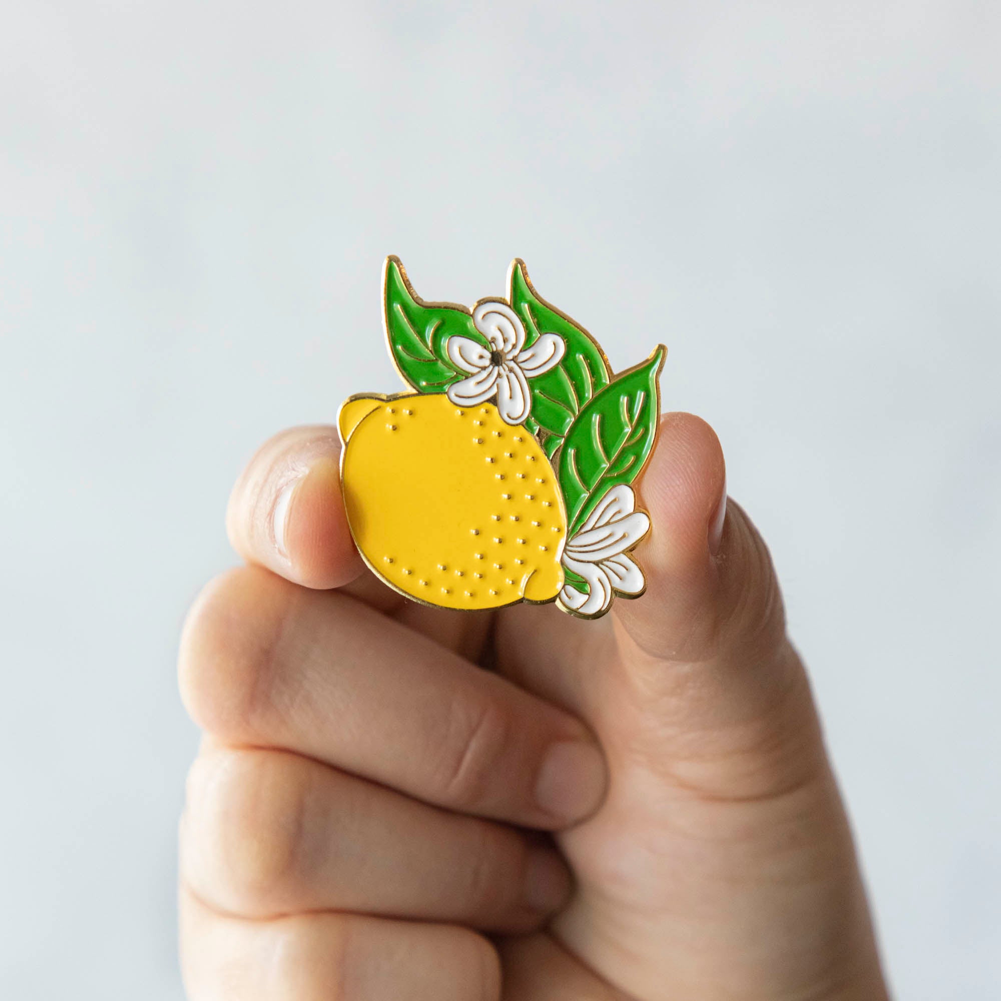A person proudly showcasing their Hester & Cook Lemon Enamel Pin, a vibrant accessory inspired by fresh fruits.
