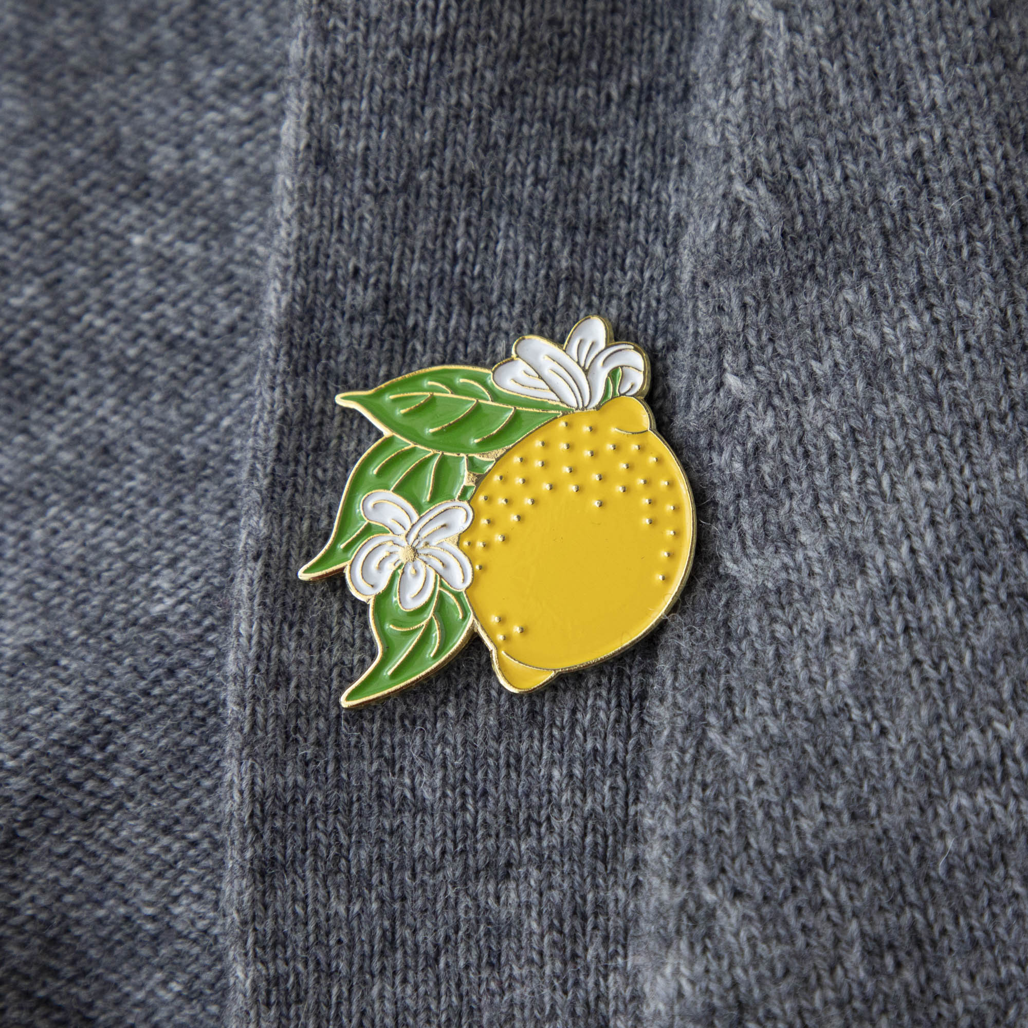 A Lemon Enamel Pin from Hester &amp; Cook adorns the front of a stylish gray sweater.