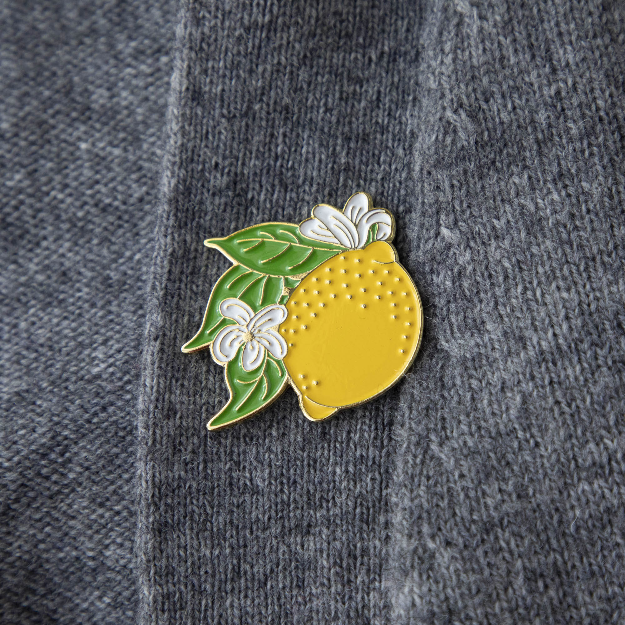 A Lemon Enamel Pin from Hester & Cook adorns the front of a stylish gray sweater.