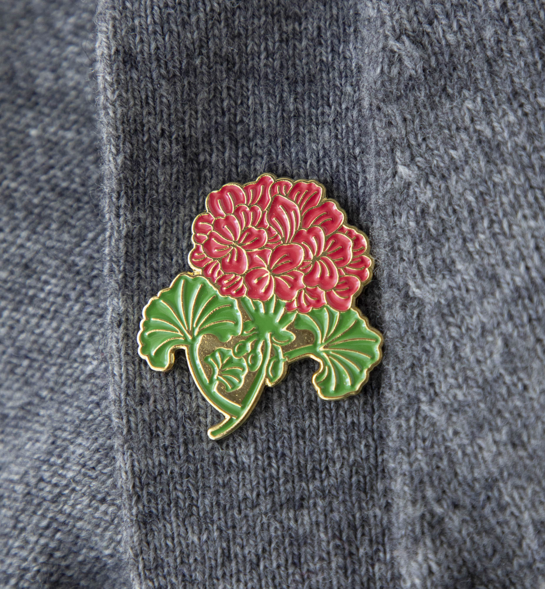 An enchanting Hester & Cook Geranium Enamel Pin with a beautiful red Geranium flower delicately paired with green foliage.