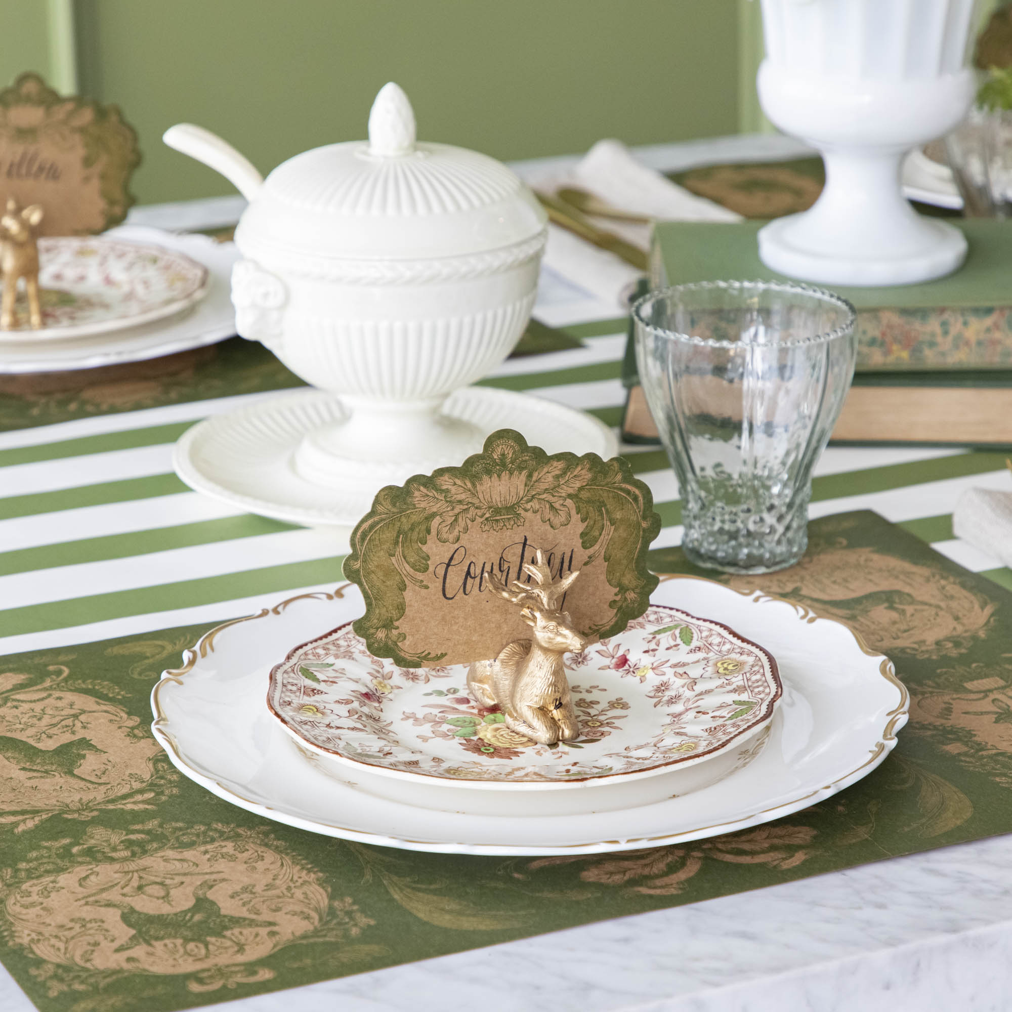An elegant table setting with the Deer Place Card Holder holding the Moss Fable Toile Place Card with the name "Courtney" written in cursive, and the Moss Fable Toile Placemat underneath.