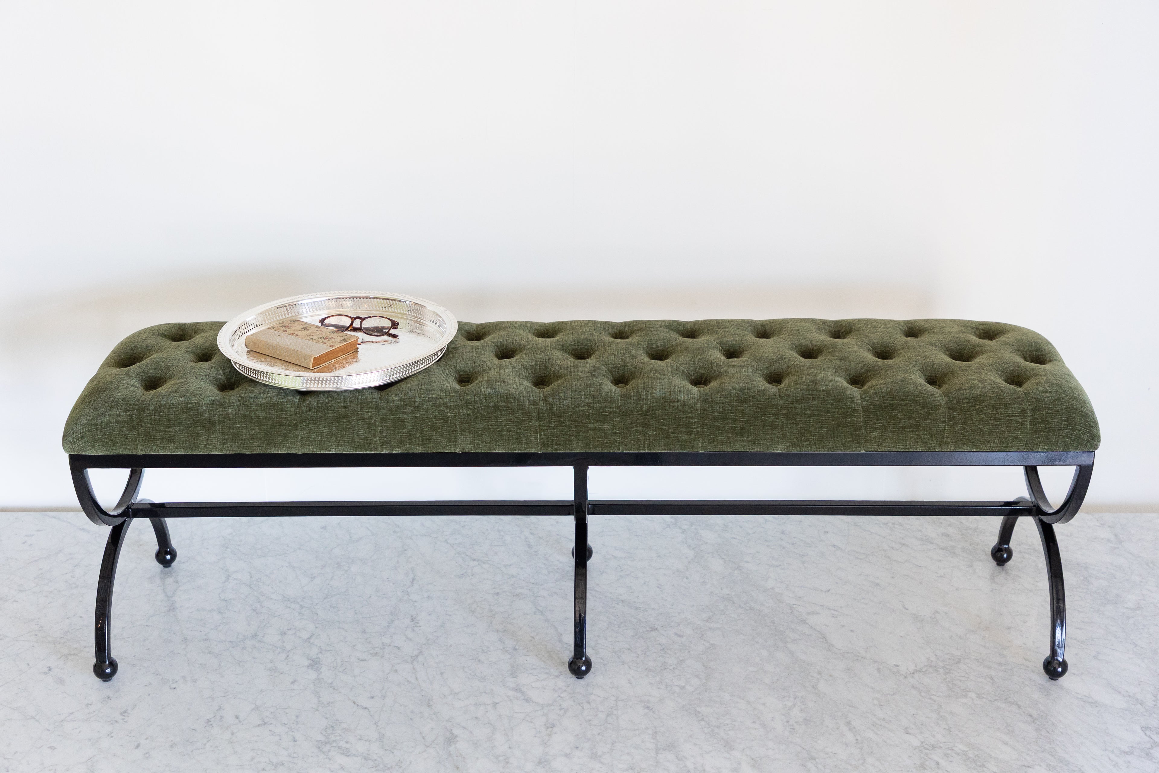 Green tufted bench with black metal legs on a white background