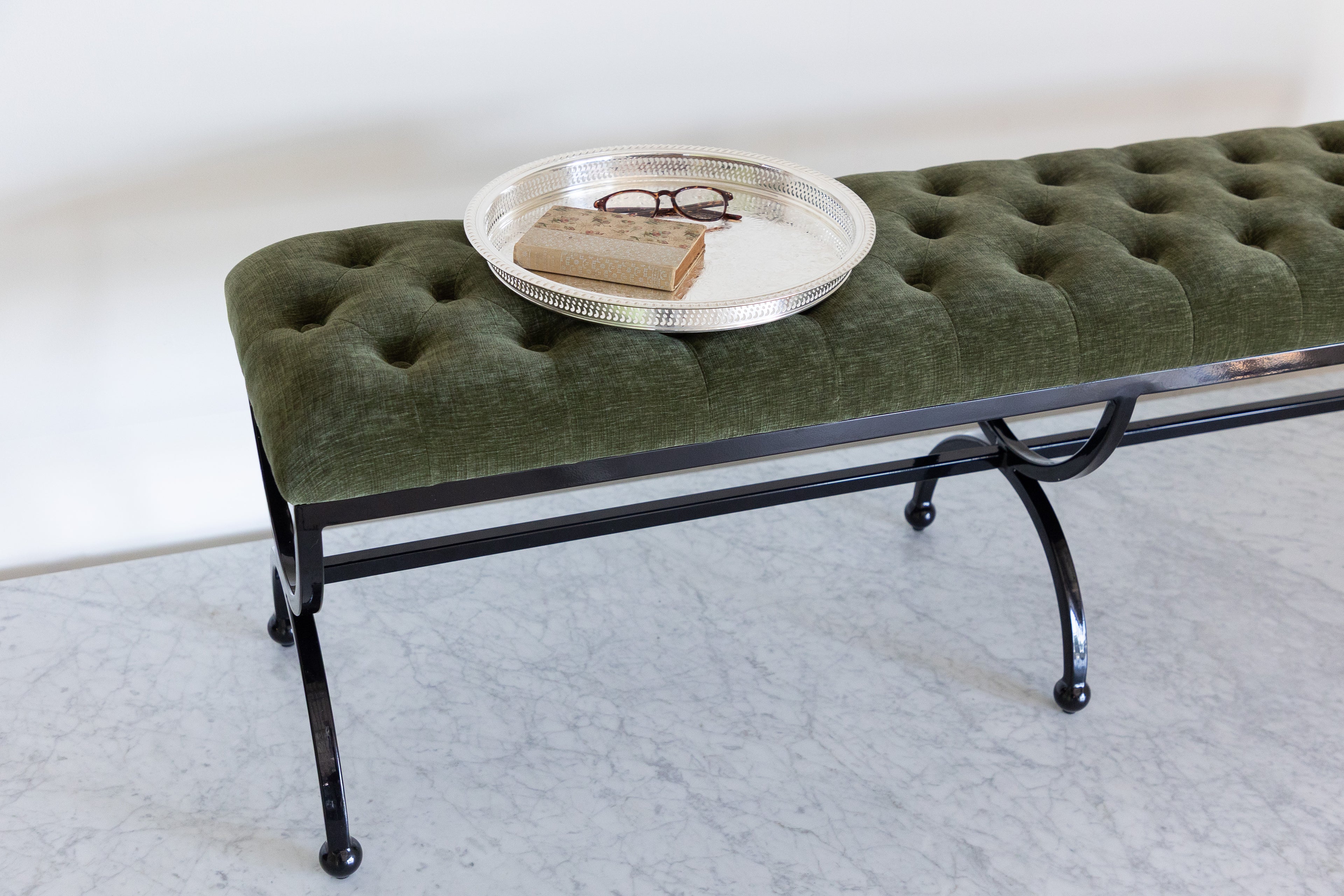 Green upholstered bench with a round metal tray on a white background