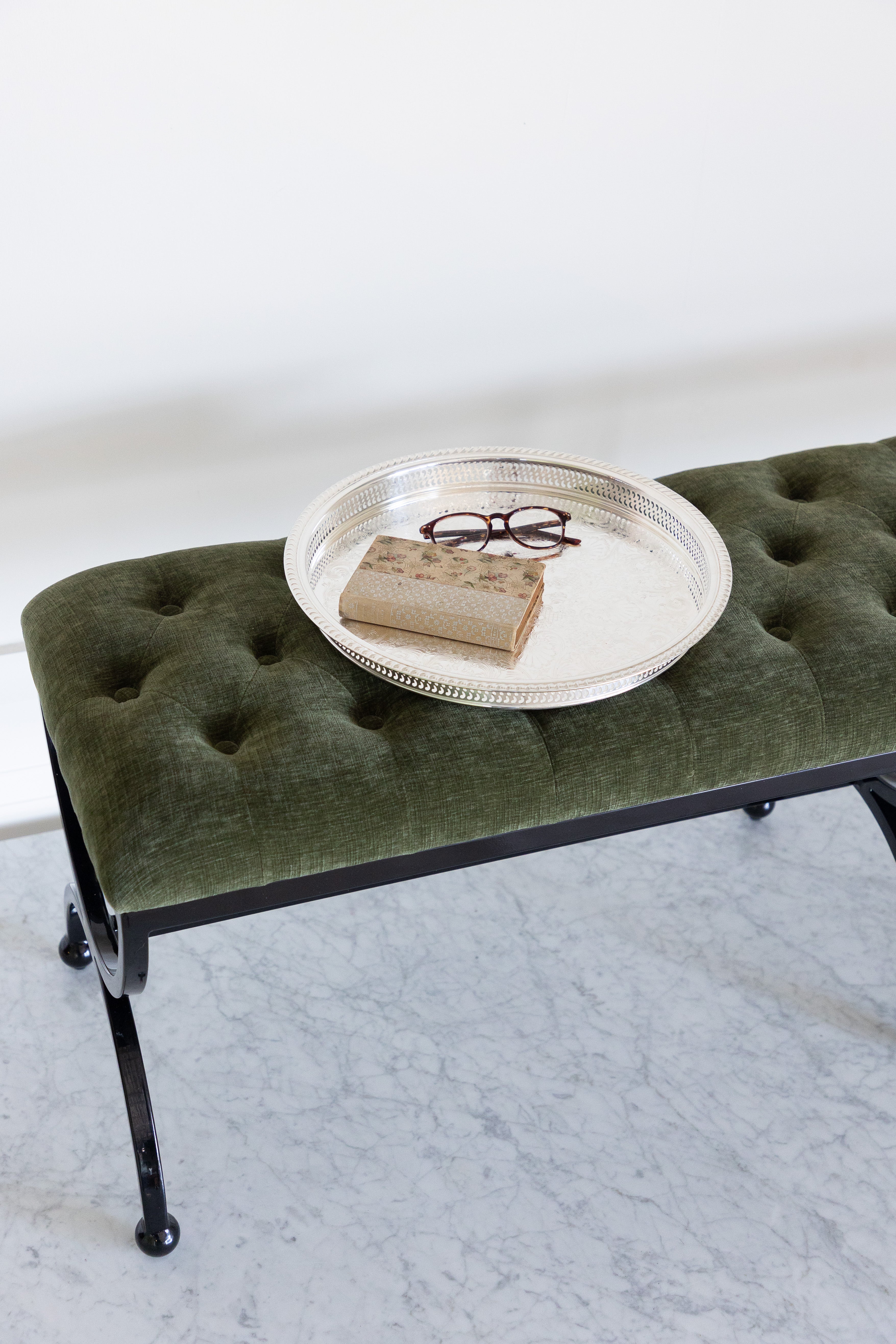 Green upholstered bench with a round metal tray on a white background