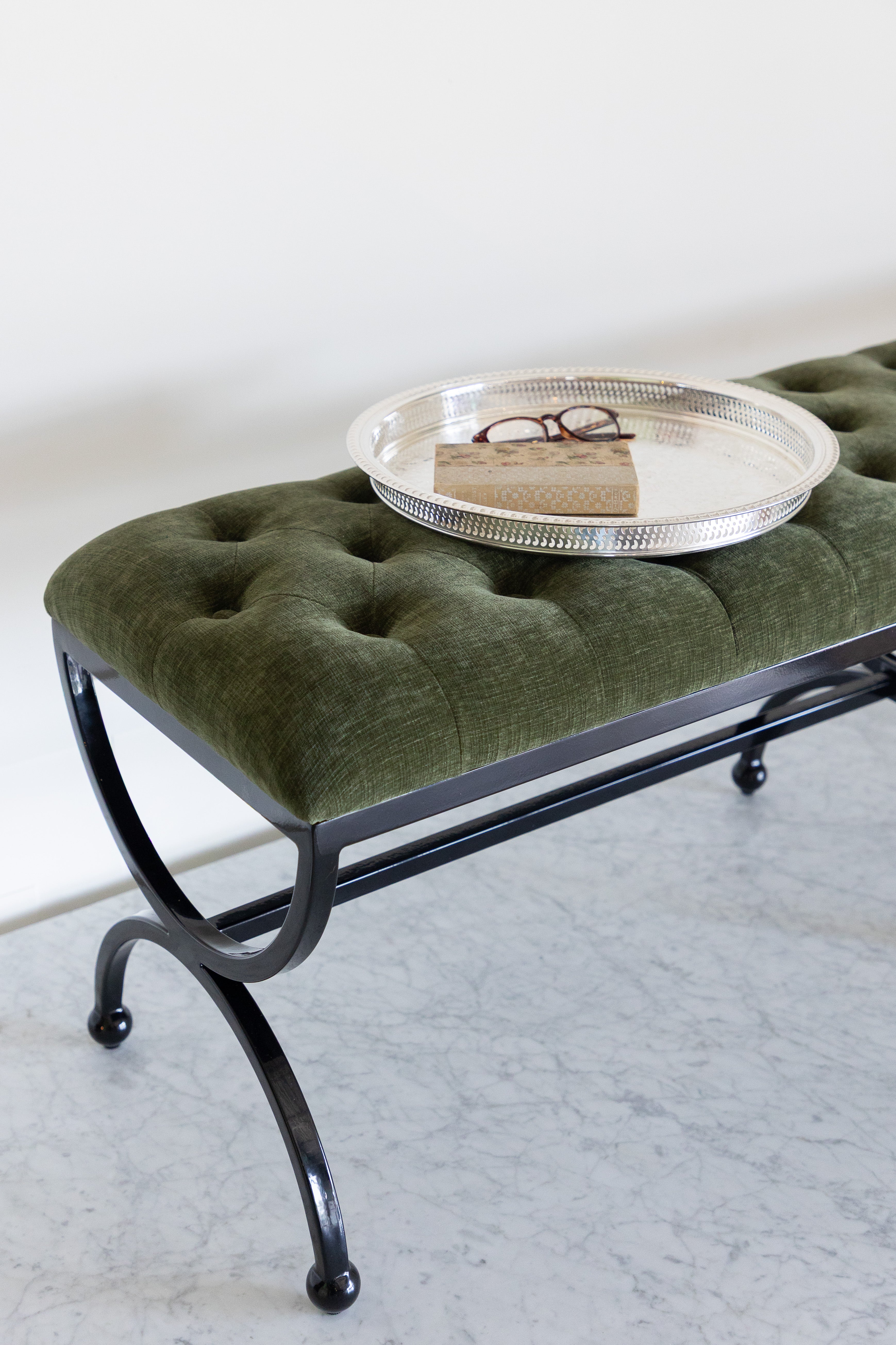 Green upholstered bench with a black metal frame on a light gray floor.
