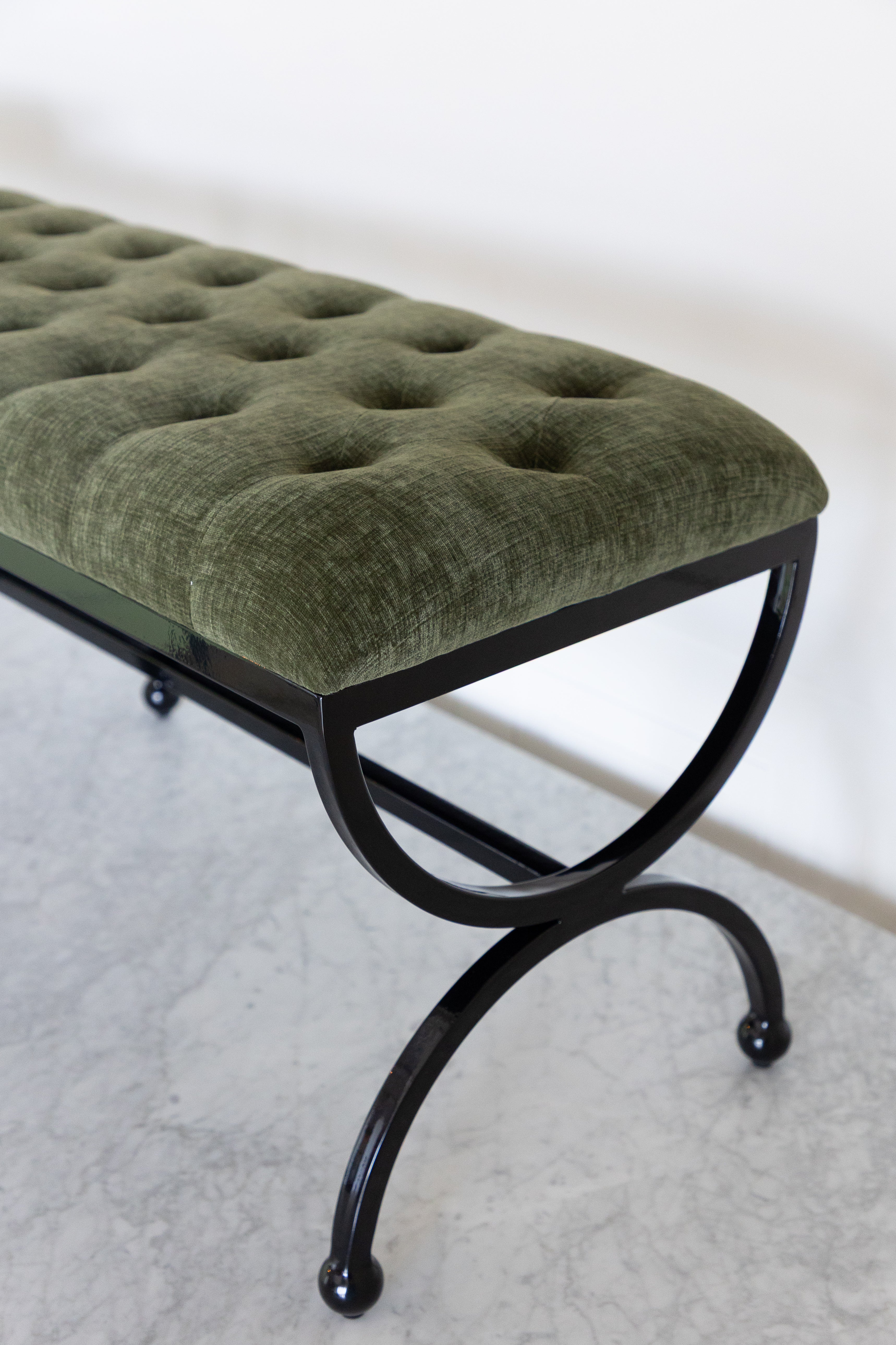 Green upholstered bench with black metal legs on a light gray floor.