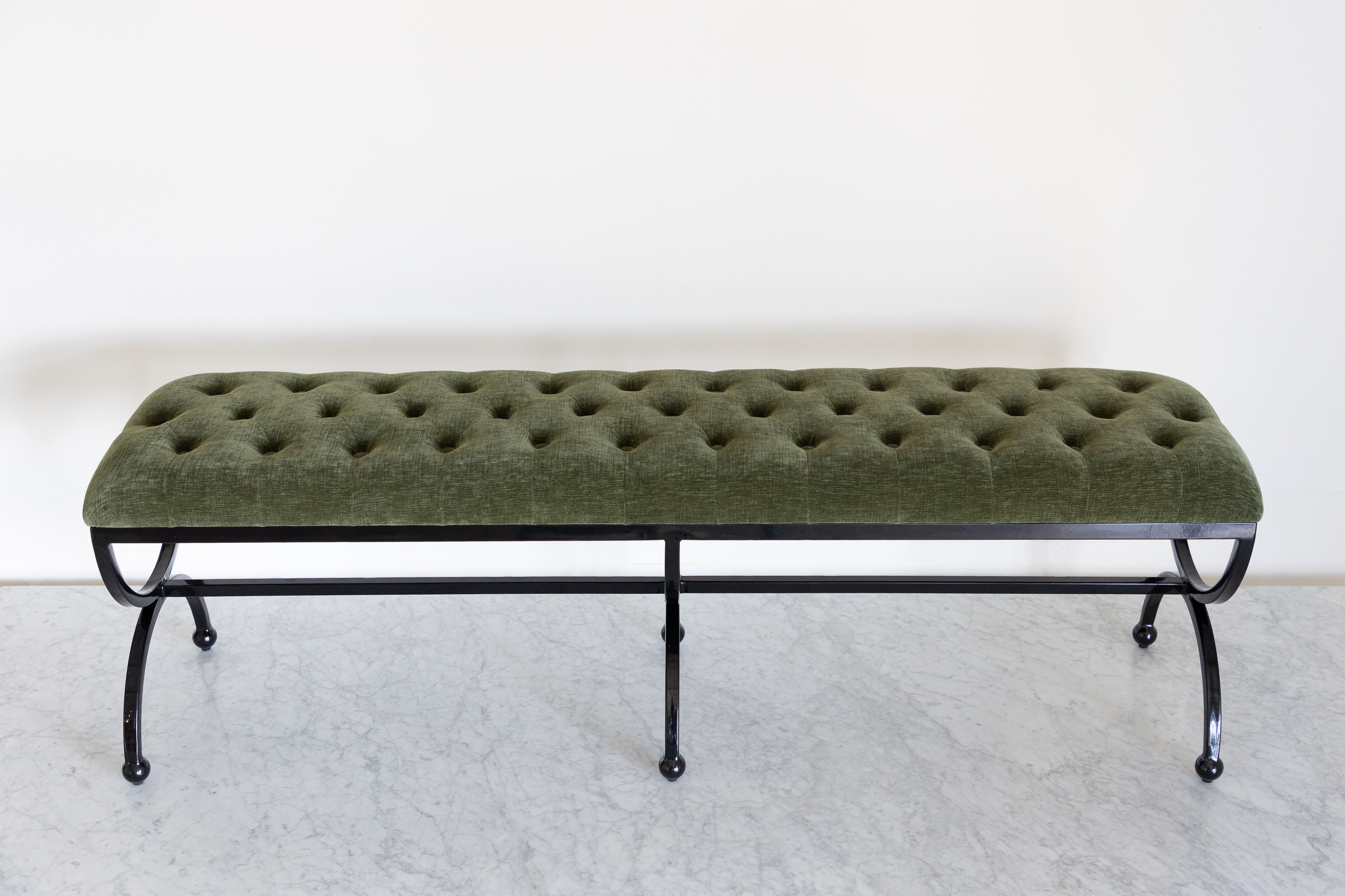 Green tufted bench with black metal legs on a white background