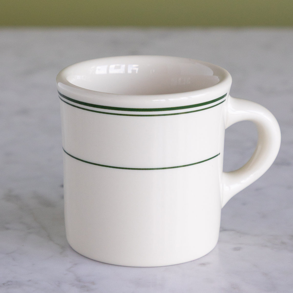 A white porcelain diner mug featuring thin green stripes near the top rim on a marble surface.
