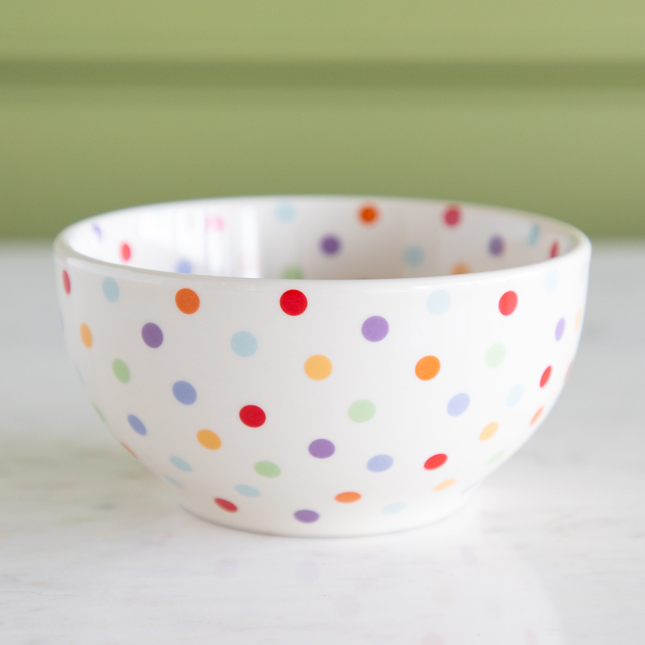 White bowl with colorful polka dot pattern on a white surface with a green background.