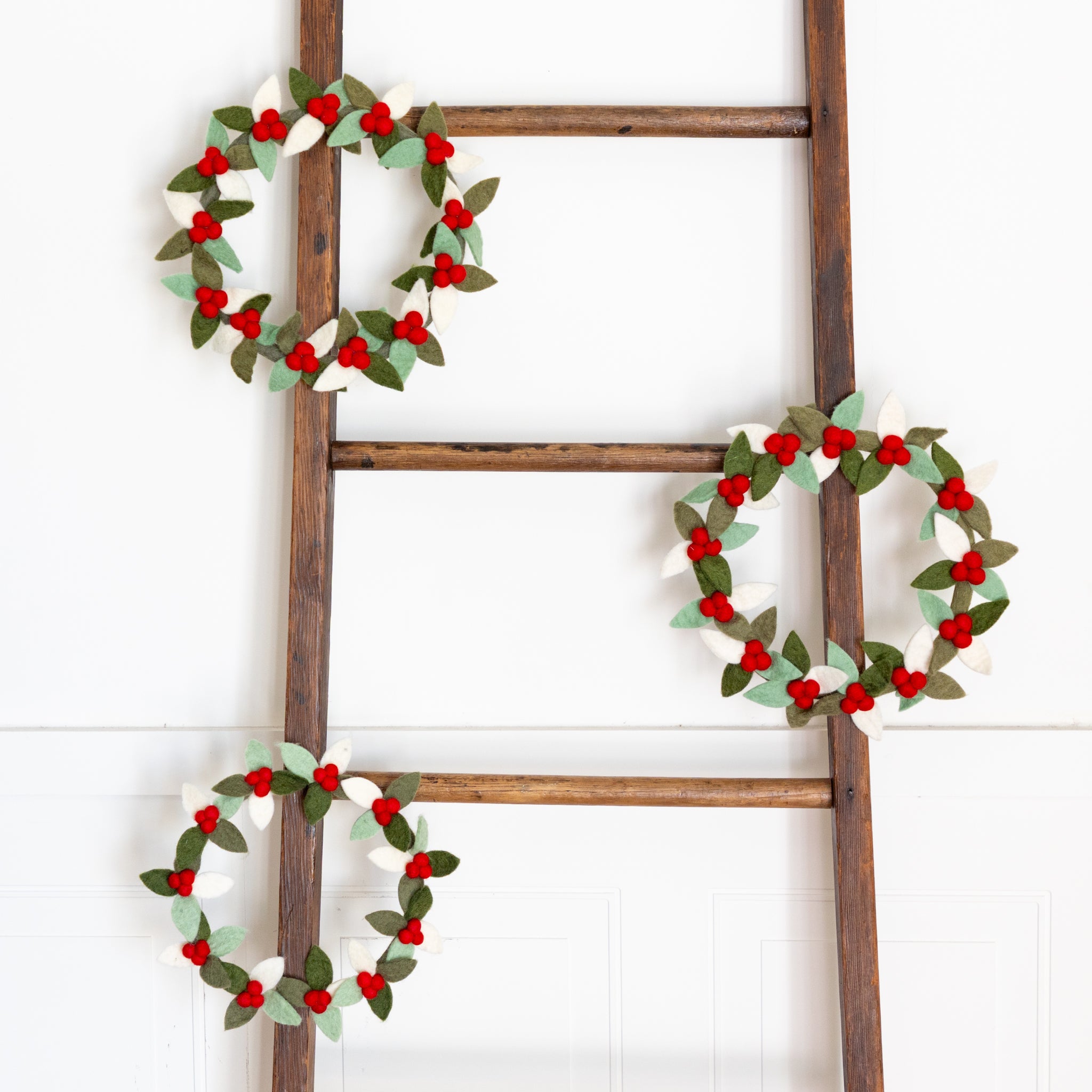 Wooden ladder with three Felt Berry Wreaths on a white background.
