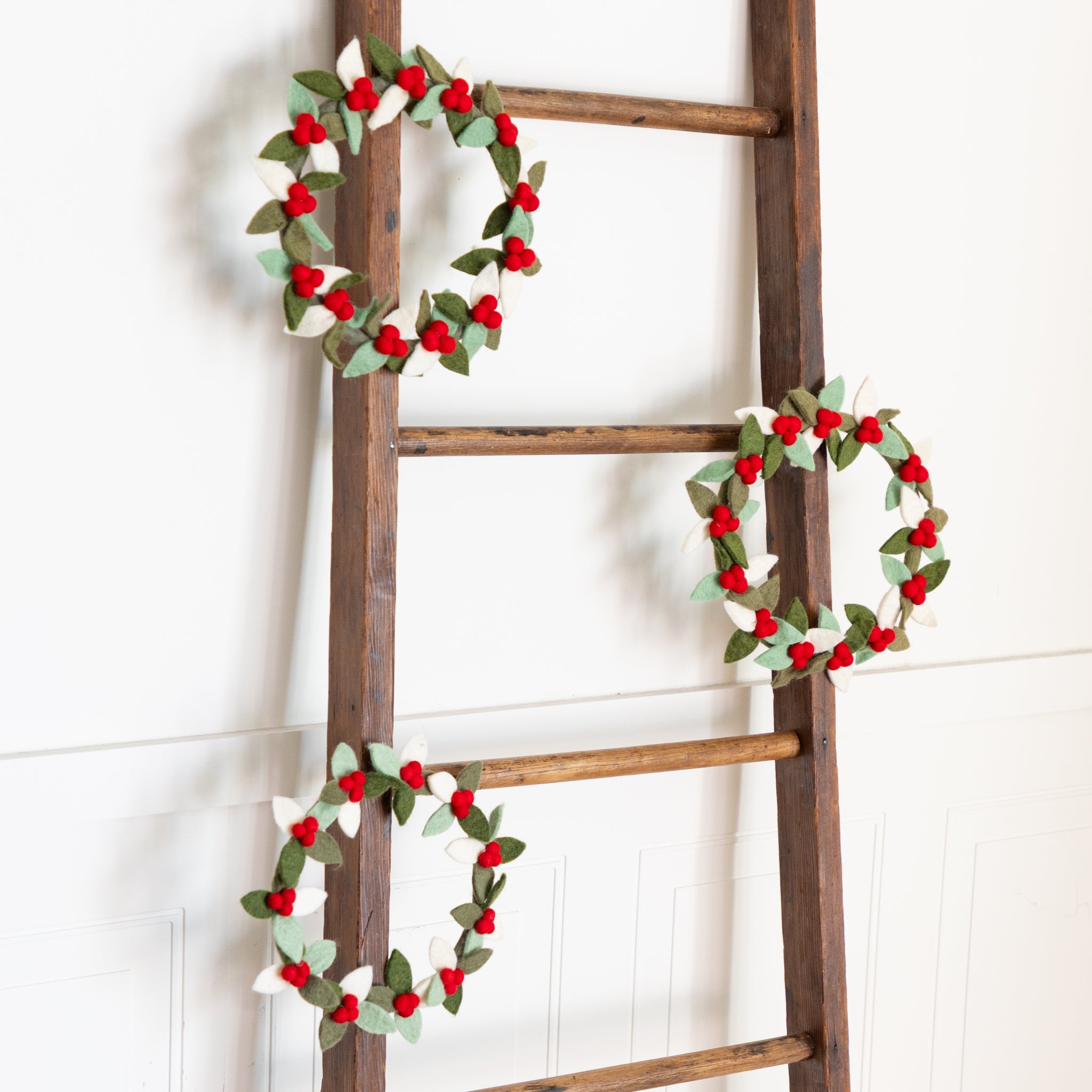 Wooden ladder with three Felt Berry Wreaths on a white background.