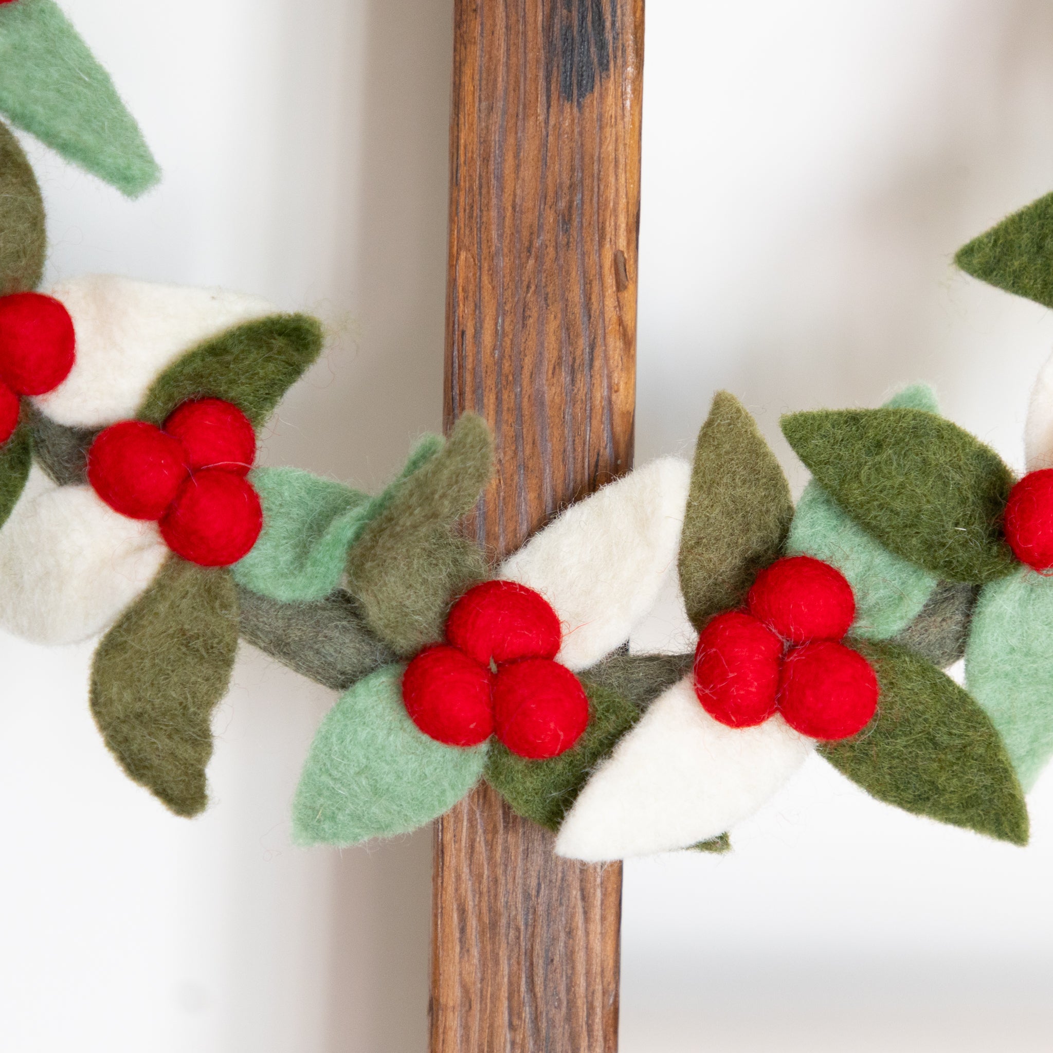 Felt holly berry wreath with green leaves and red berries on a wooden ladder.