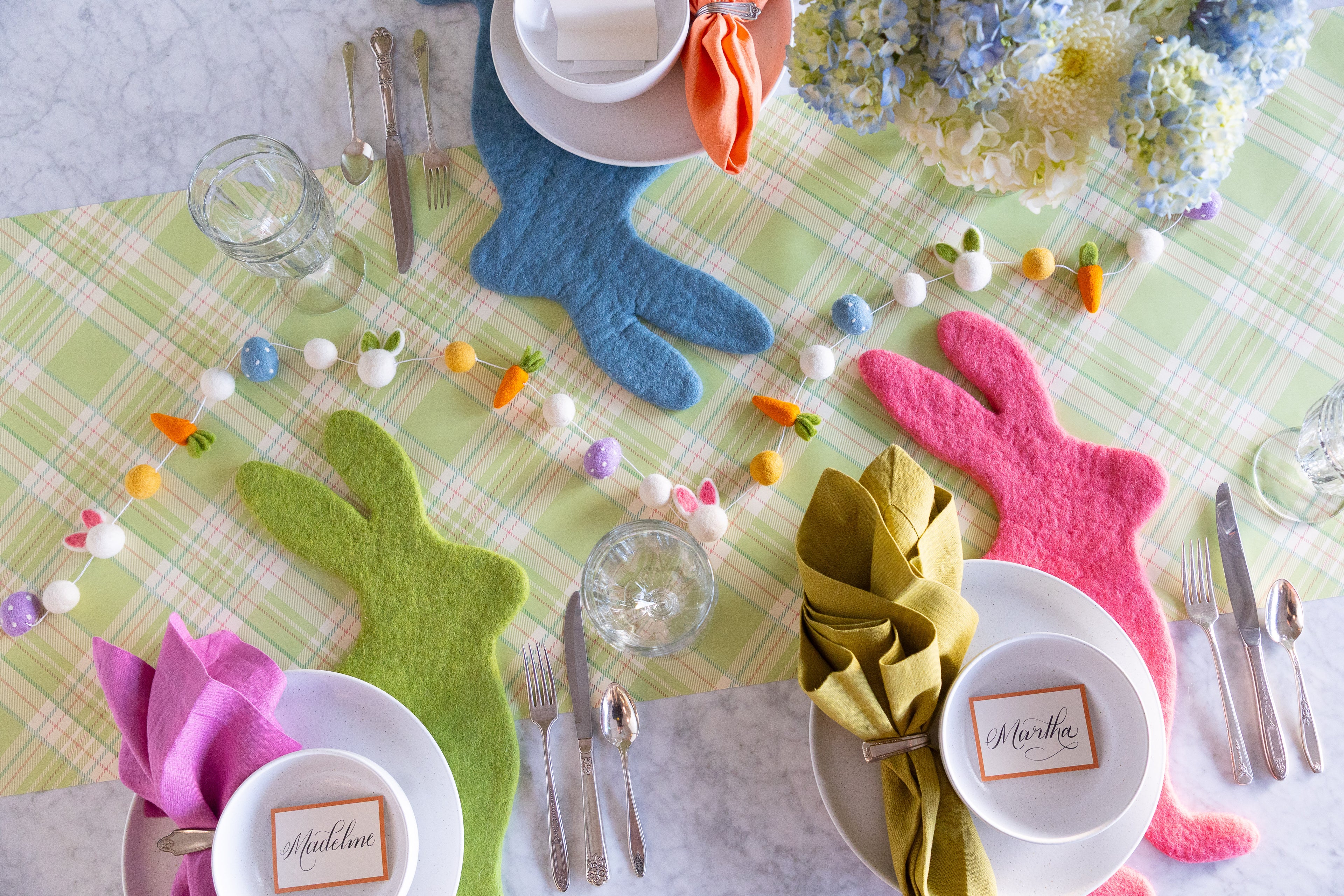 Easter themed table setting with the Cornflower Blue, Spring Green & Pink Bunny Placemats, Easter Felt Garland, Orange Frame Place Cards and dinnerware on the Green Plaid Runner.
