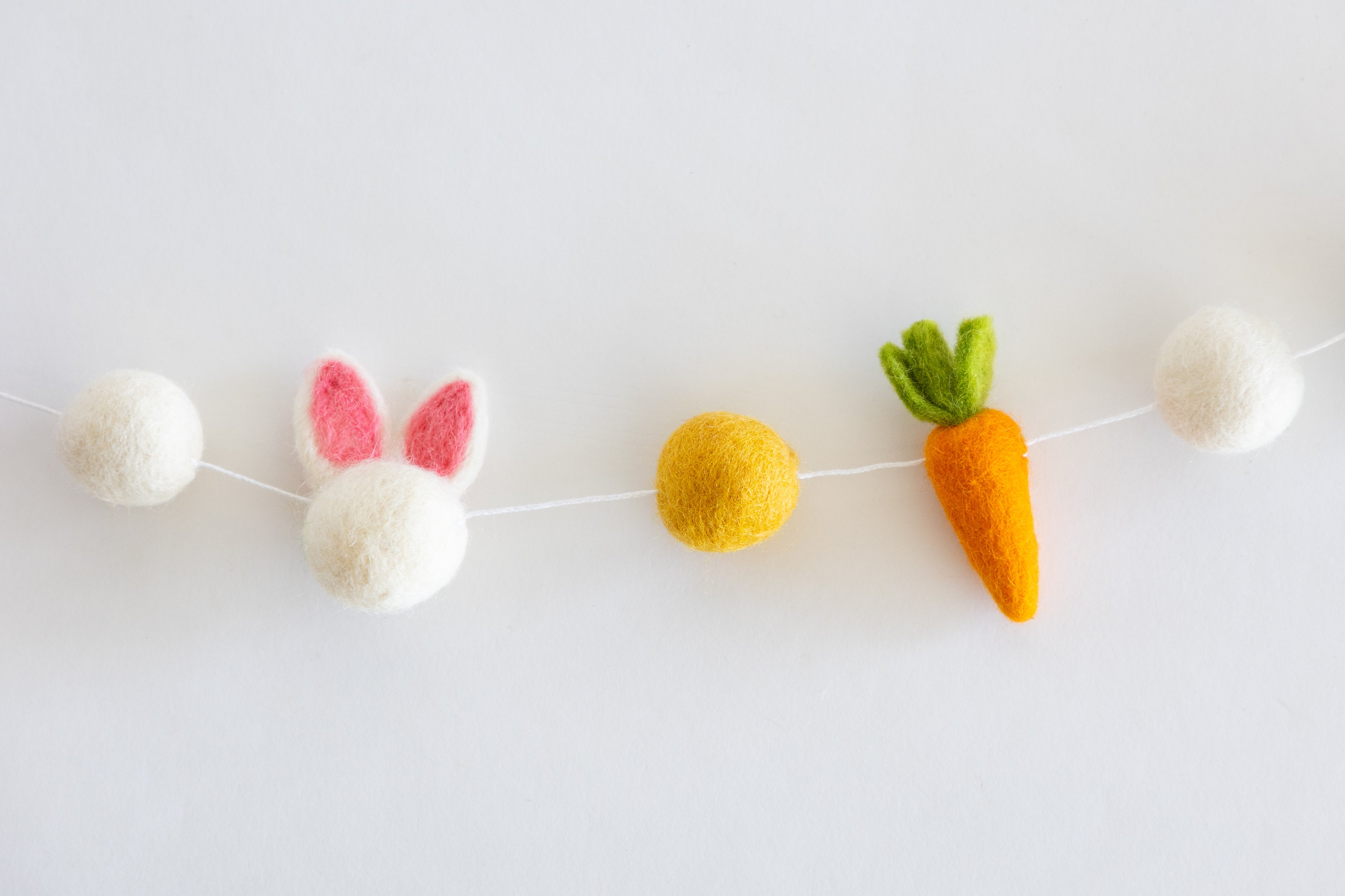 Felt Easter garland including a carrot, bunny, and eggs on a white background.