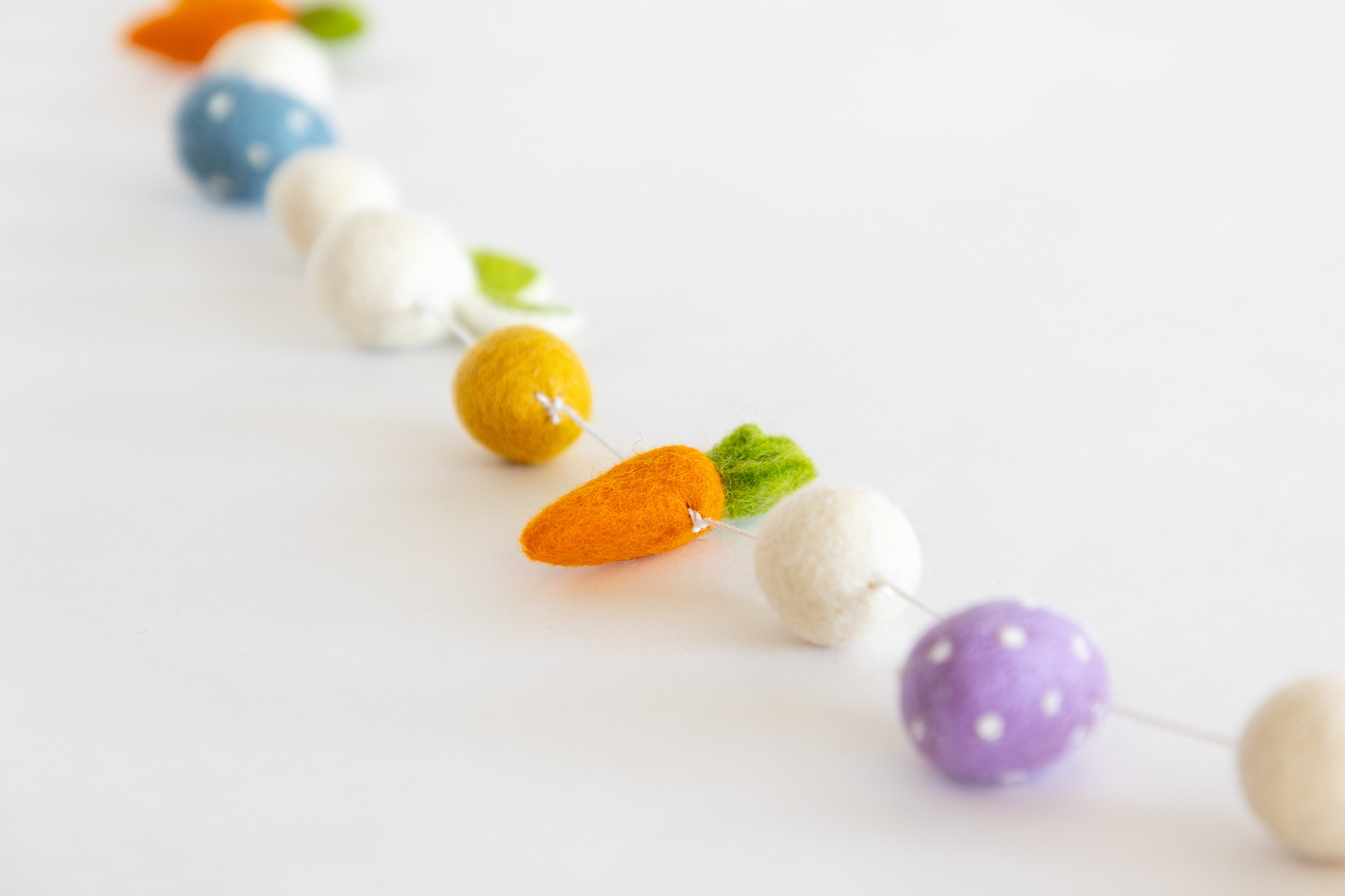 Colorful felt carrot and ball garland on a white background.