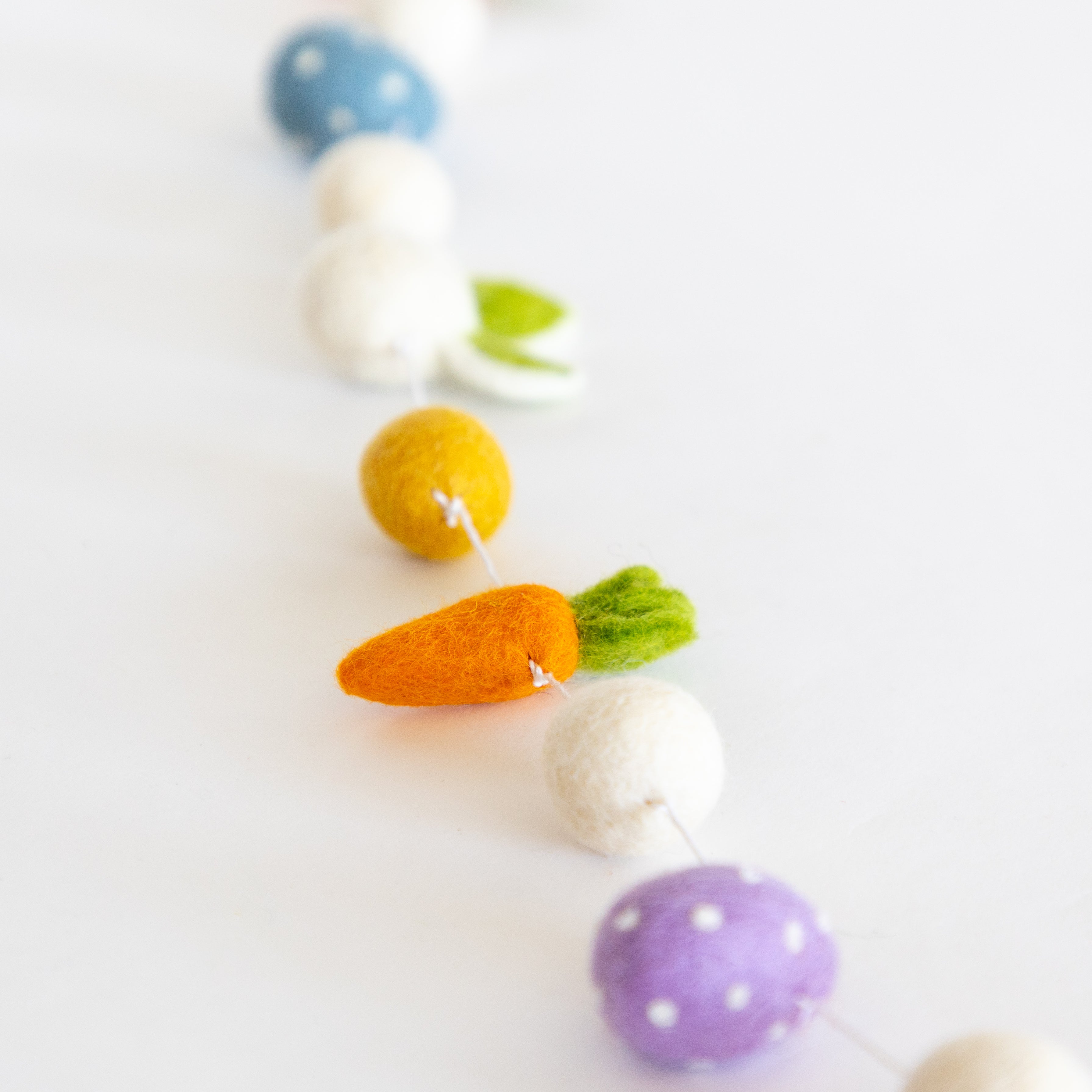 Colorful felt Easter garland with eggs and carrots on a white background.