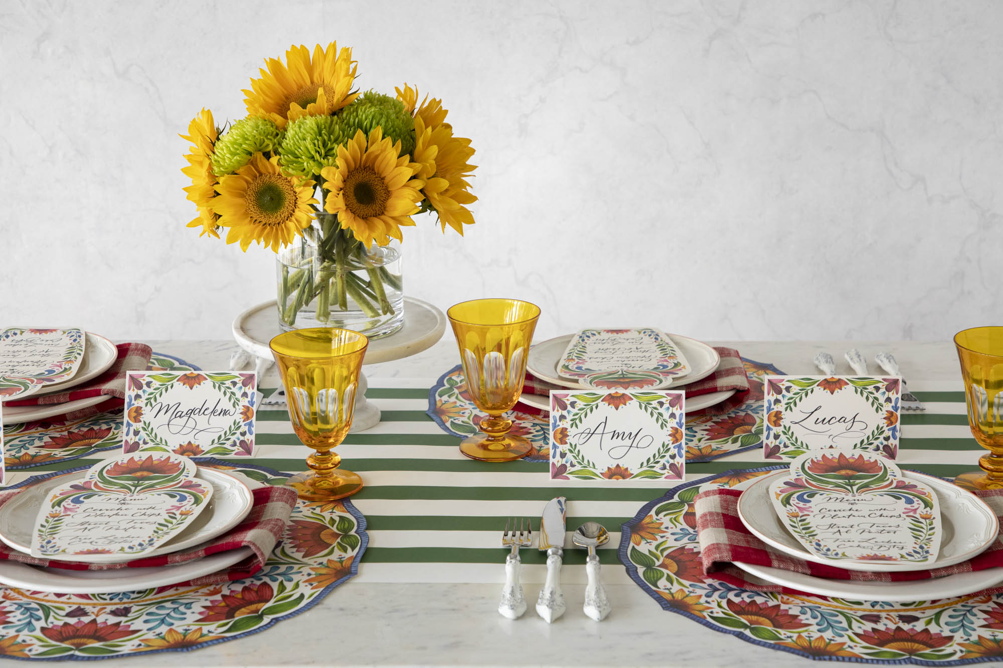 A vibrant table setting with sunflowers in a vase, accompanied by colorful Hester & Cook Die-cut Fiesta Floral Placemats.